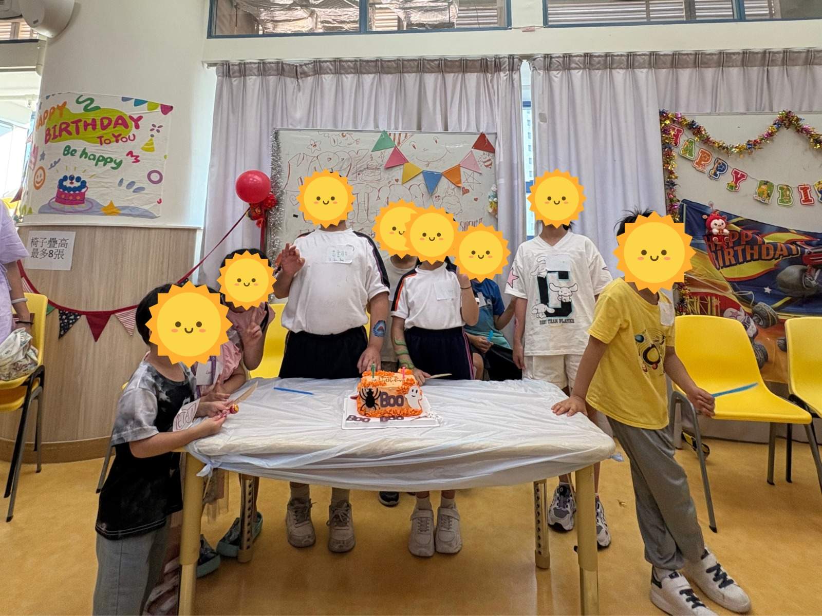 Children gathered behind a decorated birthday cake on a table.