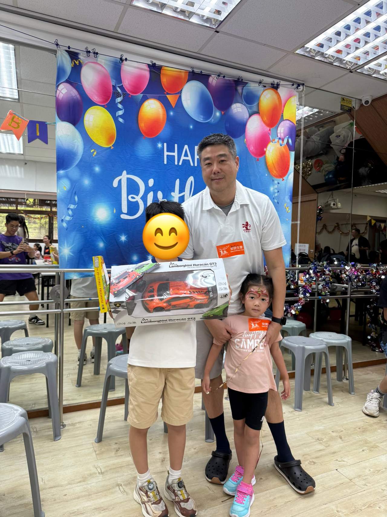 An adult stands behind two children holding gifts.