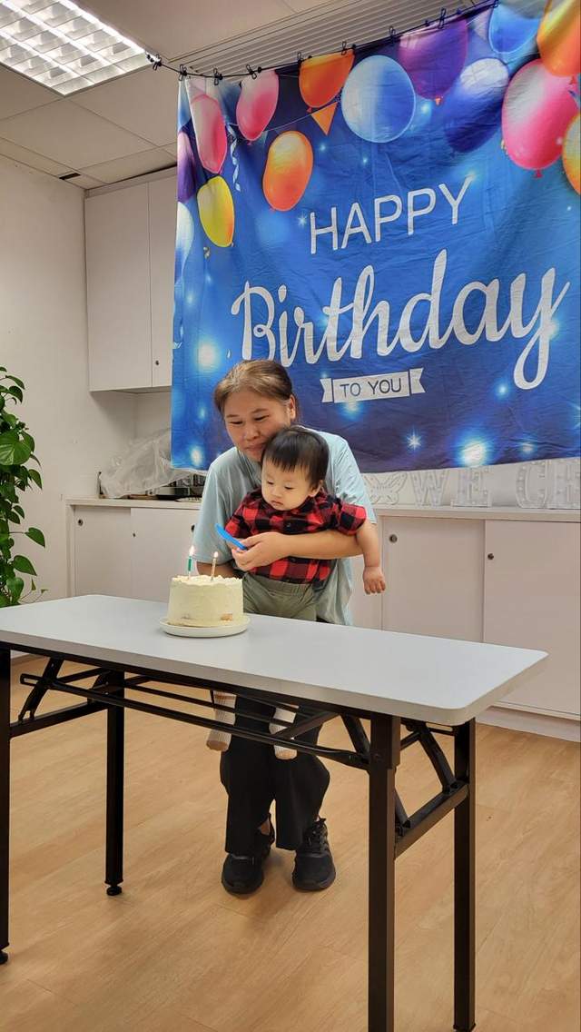 A child stands behind a cake table beneath a balloon backdrop.