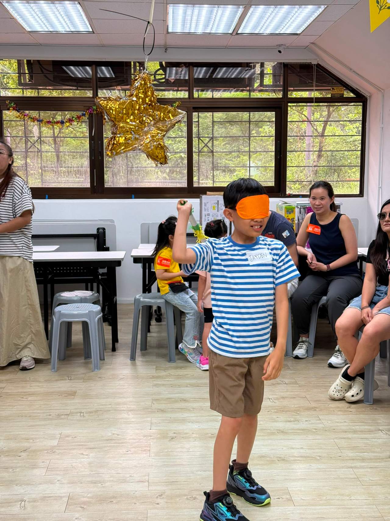 A child stands blindfolded while seated people watch.