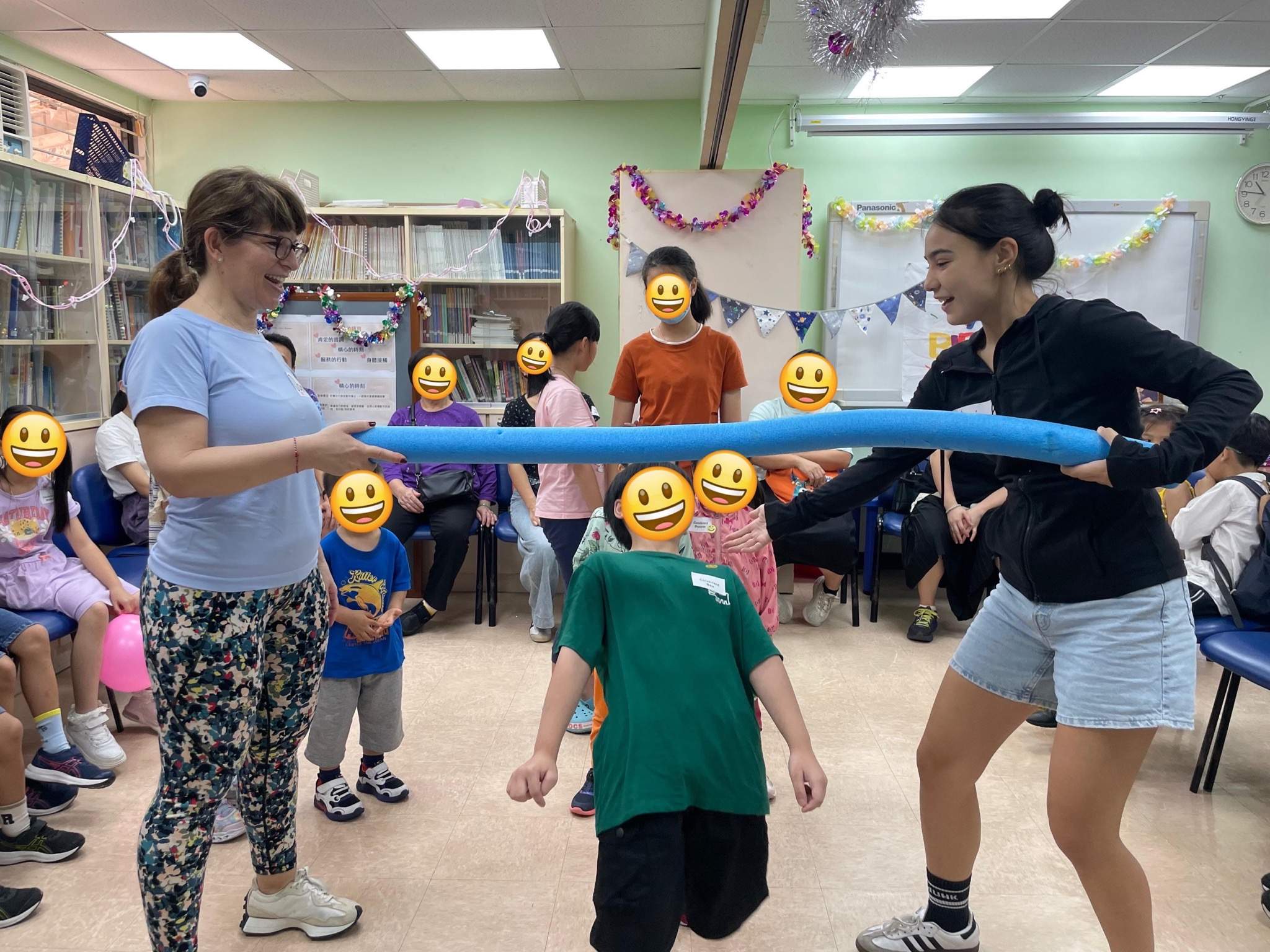 Two adults stretch a long balloon above a standing child.