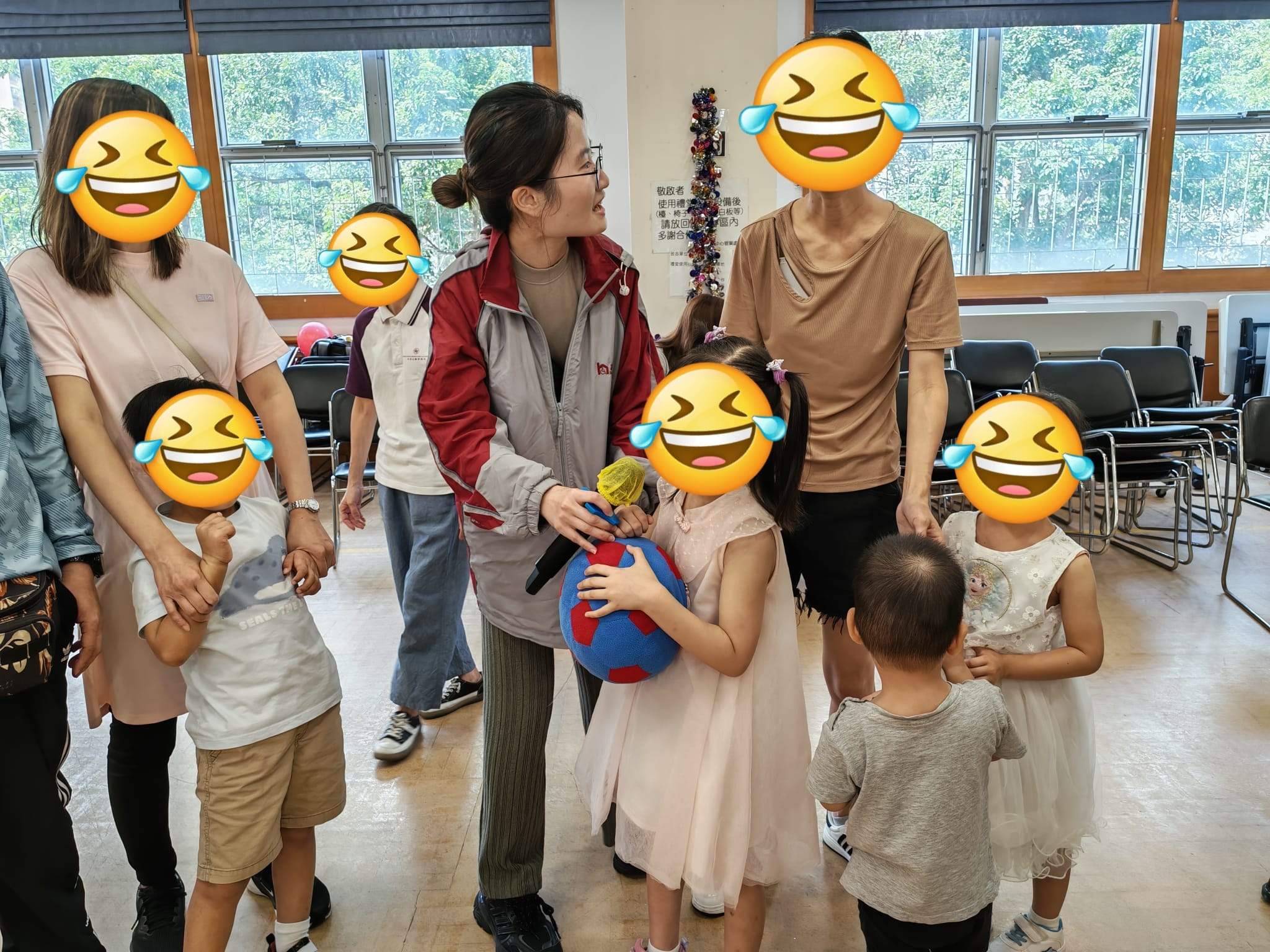 Children and adults gather around a ball during a group game.