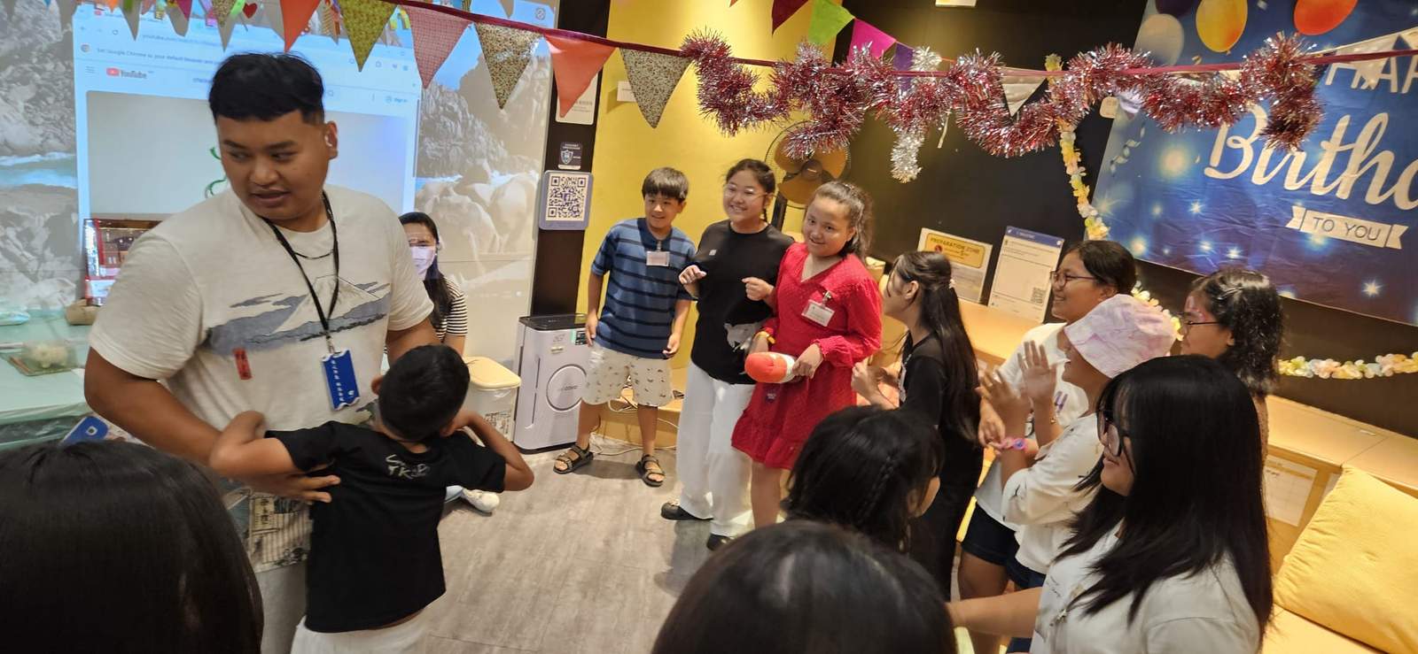 Adults and children watch an activity near the birthday backdrop.