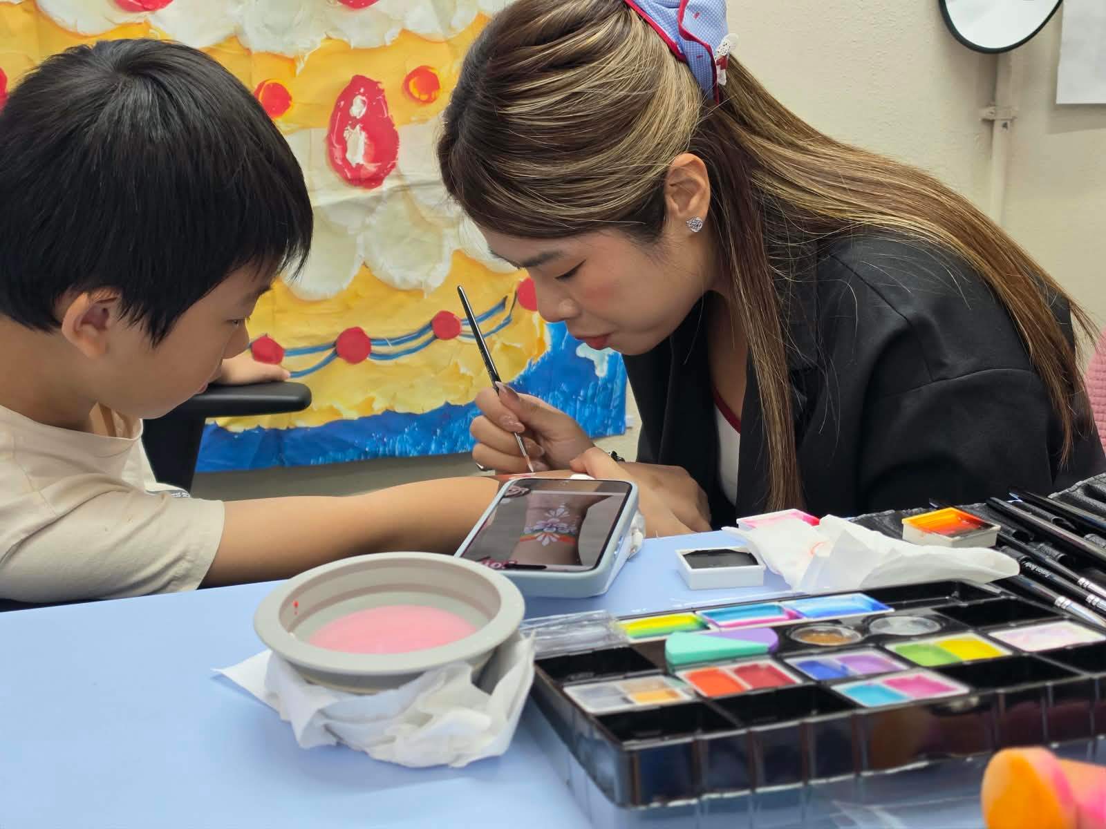 A volunteer carefully paints a design on a child's arm.
