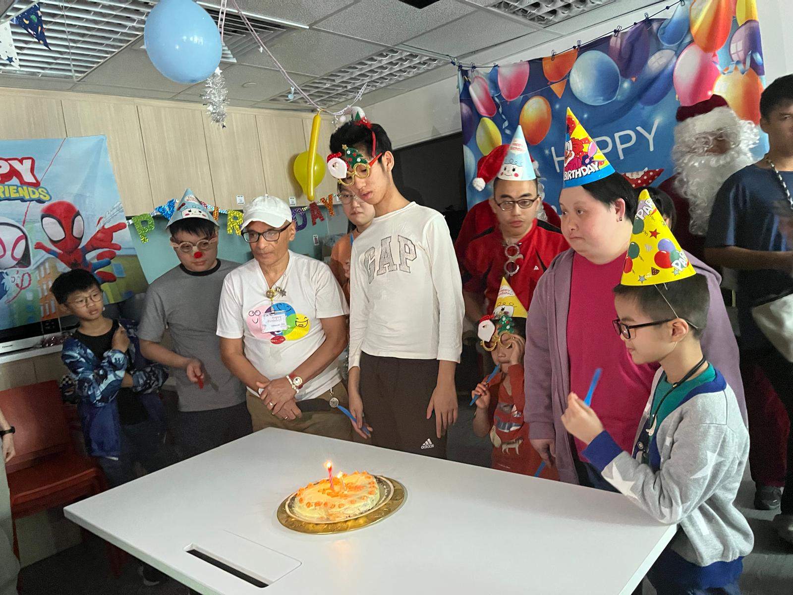 People in party hats gather around a candlelit cake.