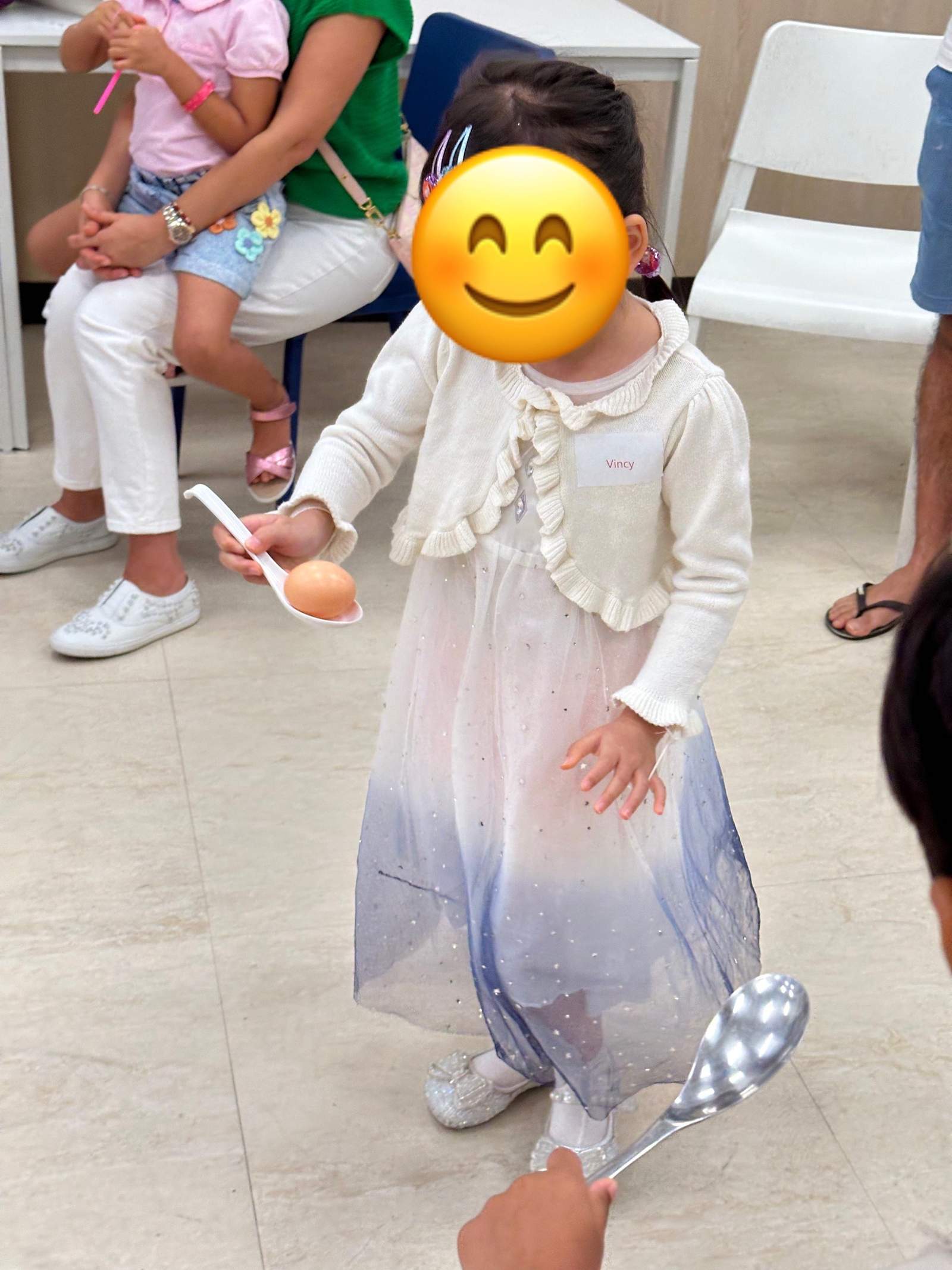 A child stands during a ball game with seated children nearby.