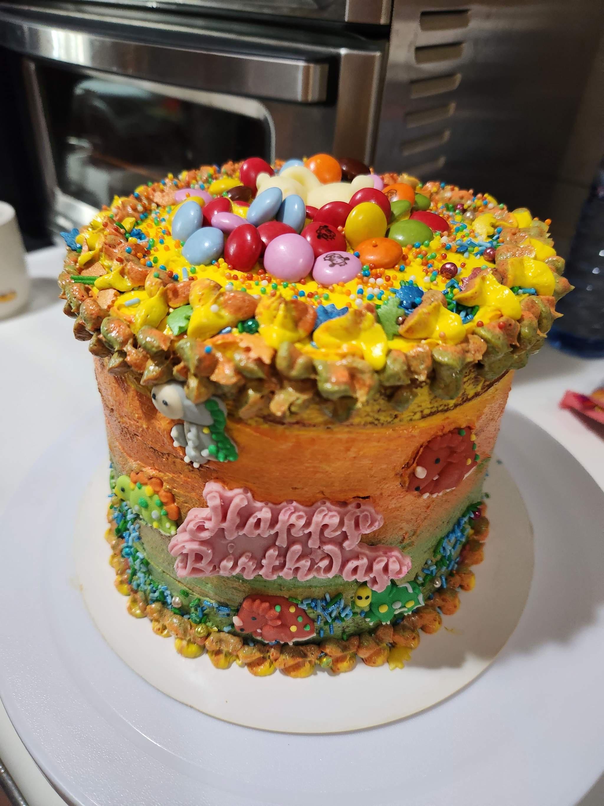A colourful dinosaur birthday cake topped with chocolate beans, by Mabel Chan.