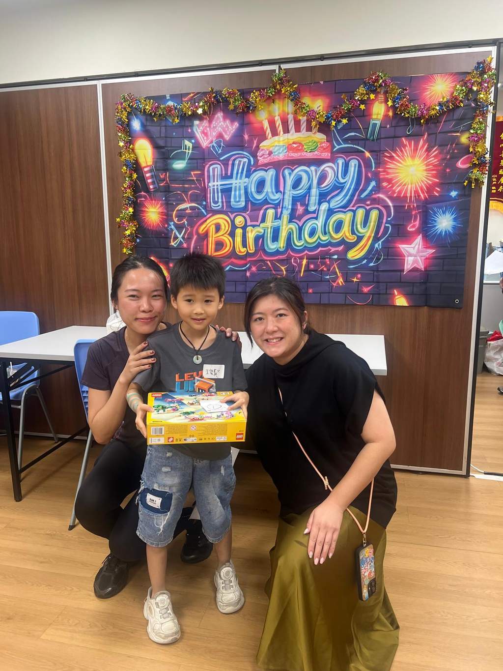 A child holds a boxed gift between two adults.