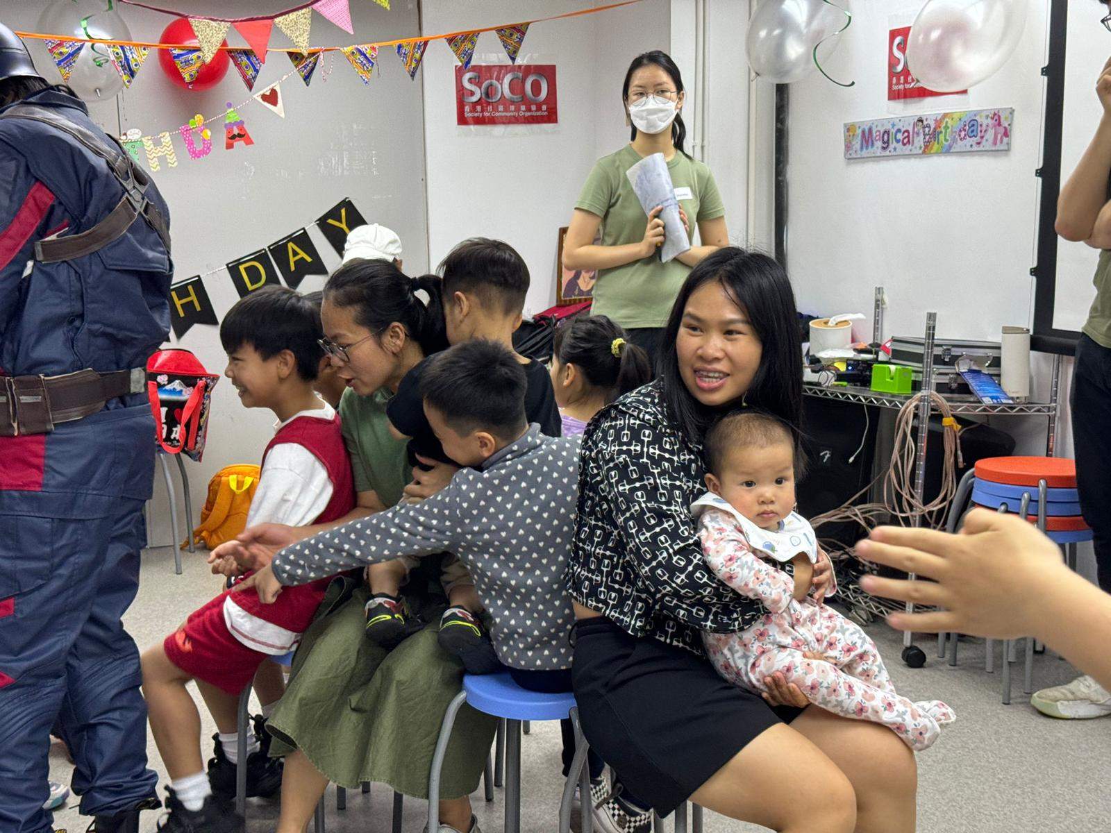 Adults and children gather closely while seated around the room.