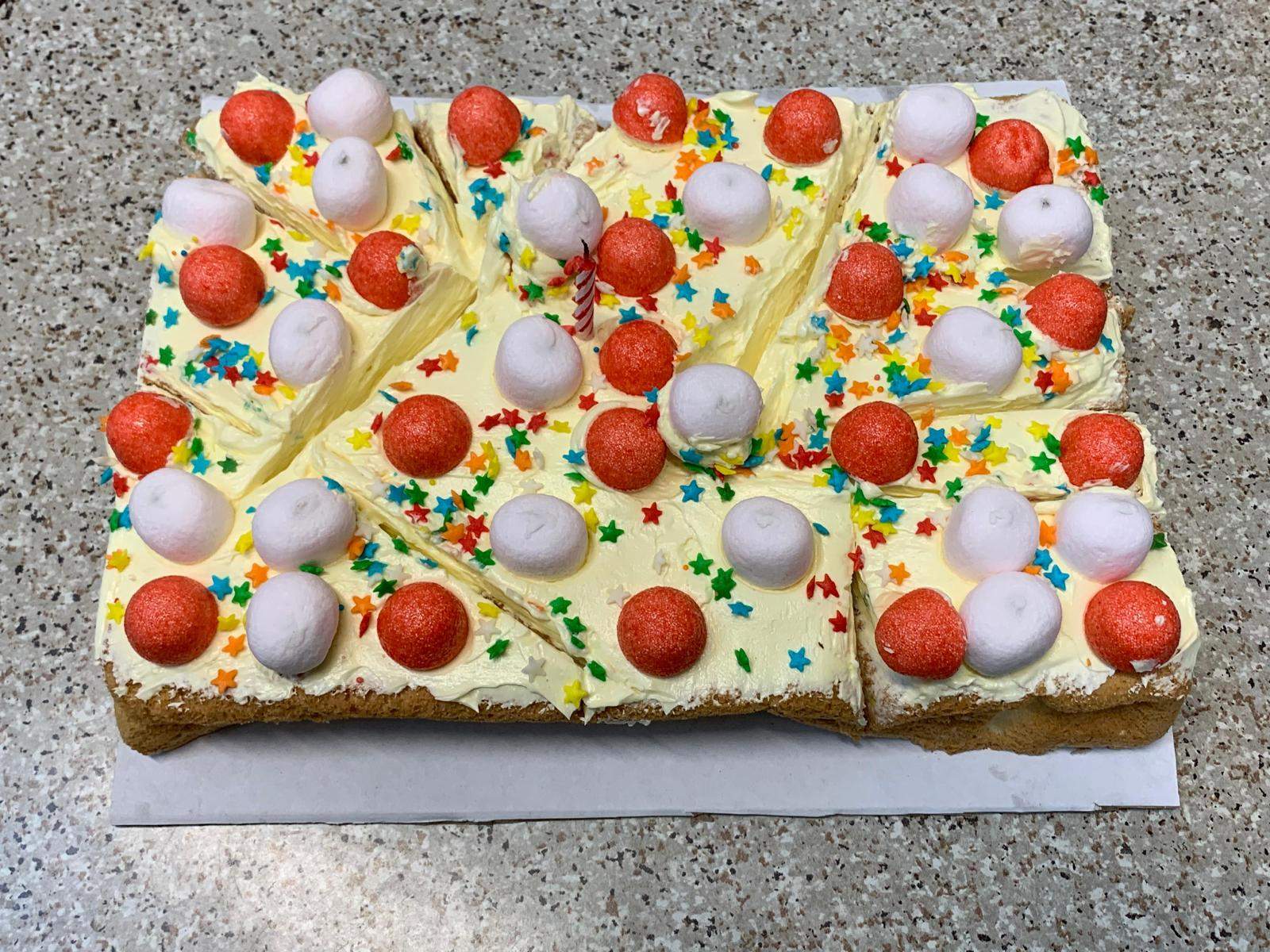 A rectangular cake is decorated with fruit and colourful sweets.