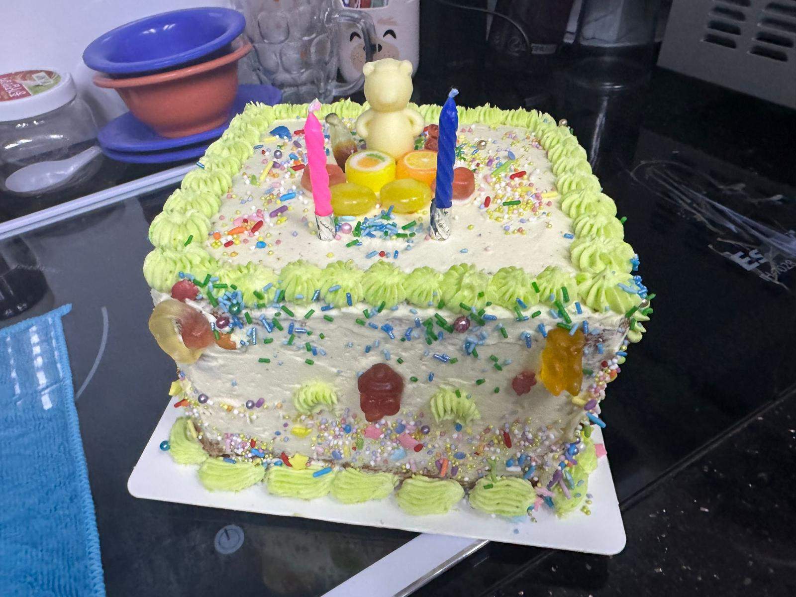 A square birthday cake is decorated with candles and green frosting.