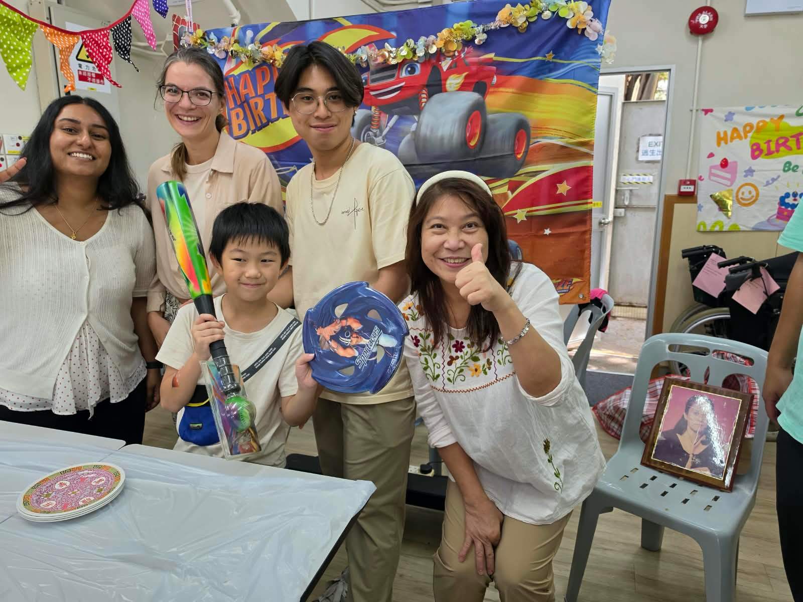 A child holds party gifts beside volunteers at the celebration.