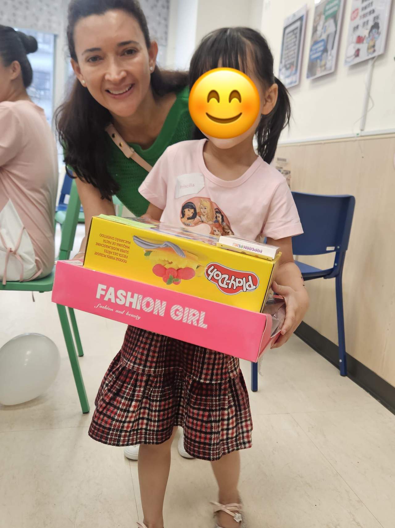 An adult kneels beside a child holding a boxed toy.