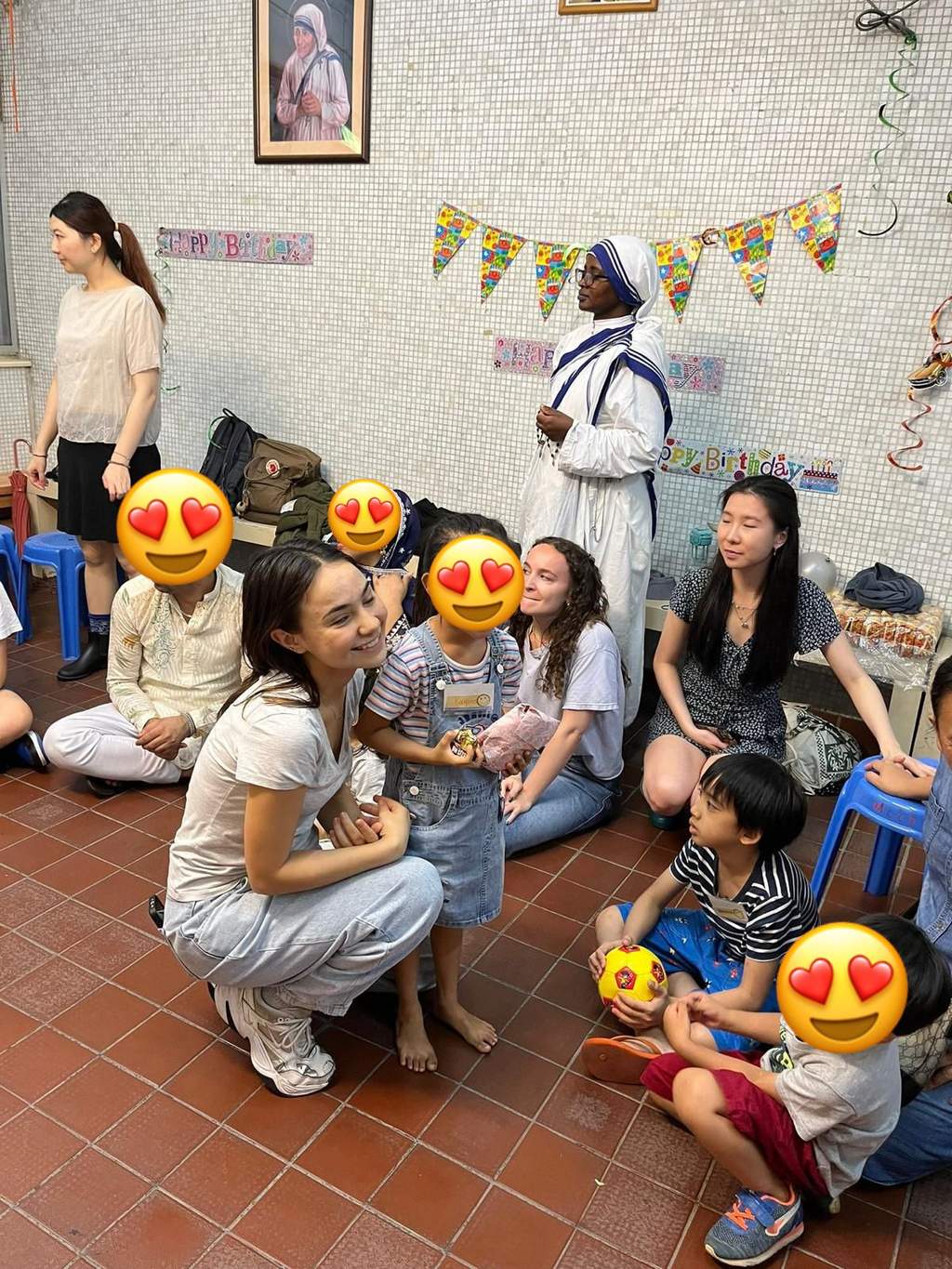 Adults kneel beside children seated around the room.