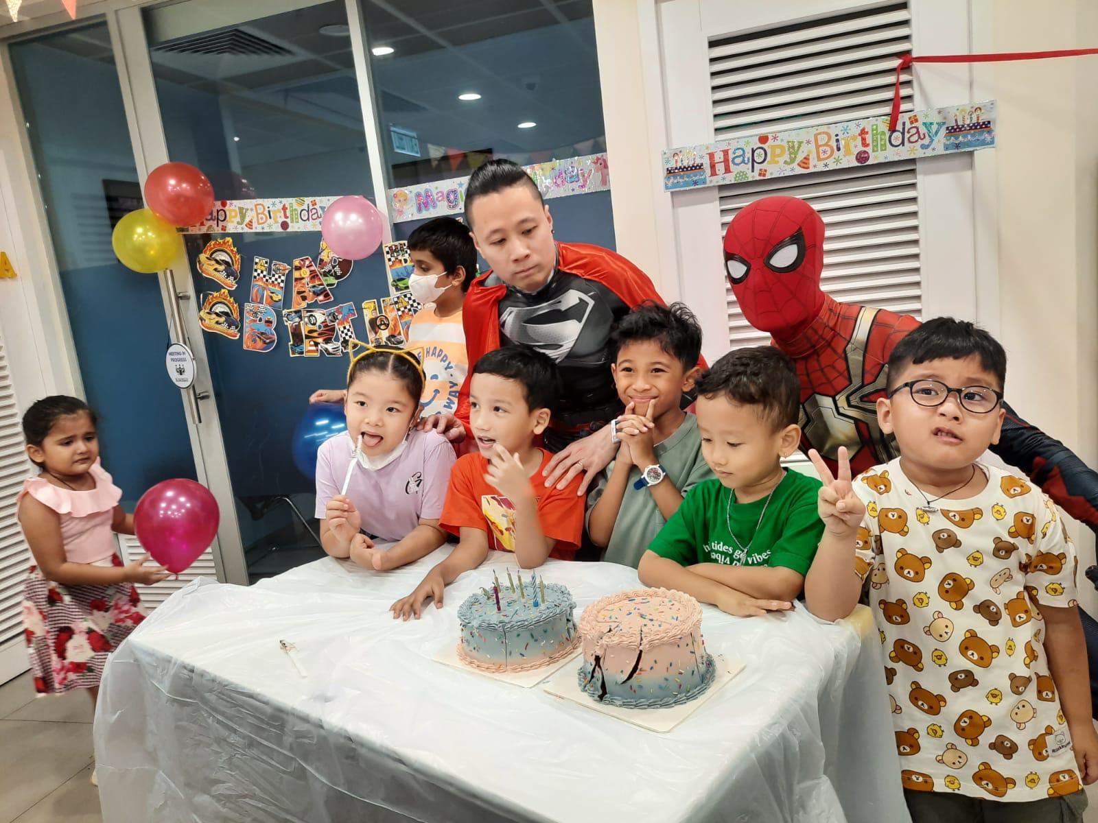 Children gather behind two cakes while costumed performers pose nearby.