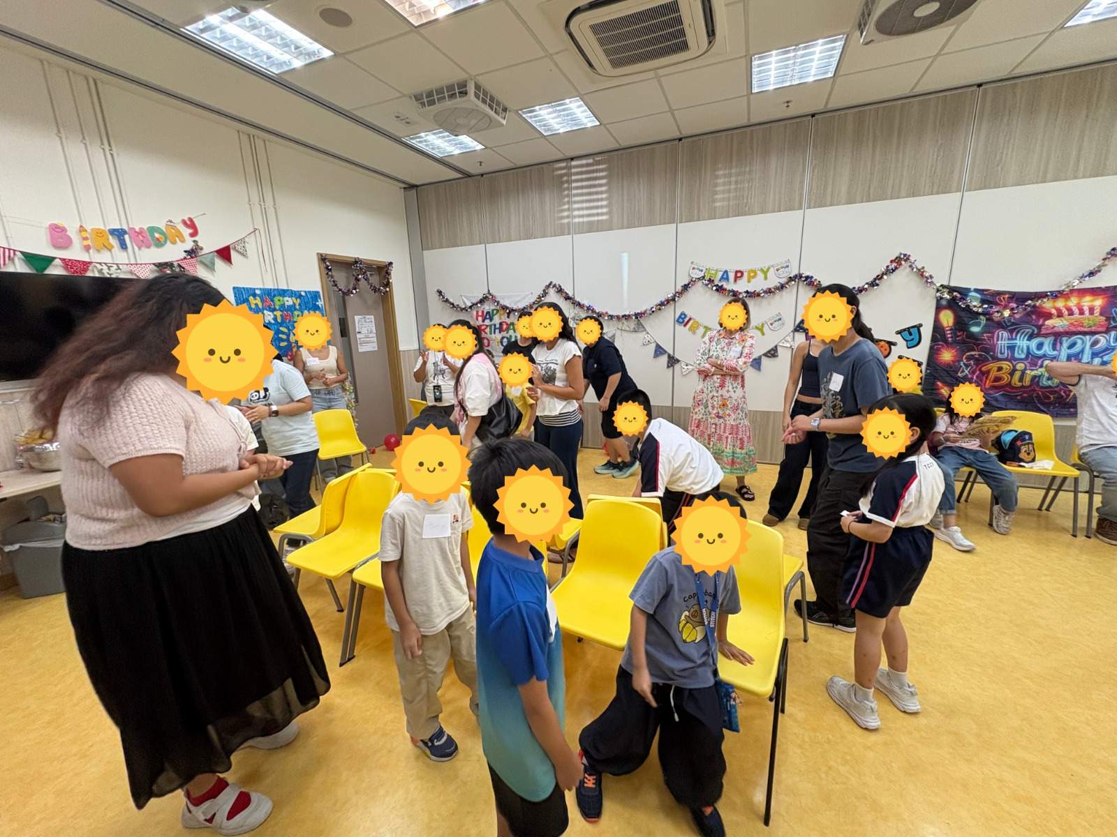 Children and volunteers playing a game among rows of yellow chairs.