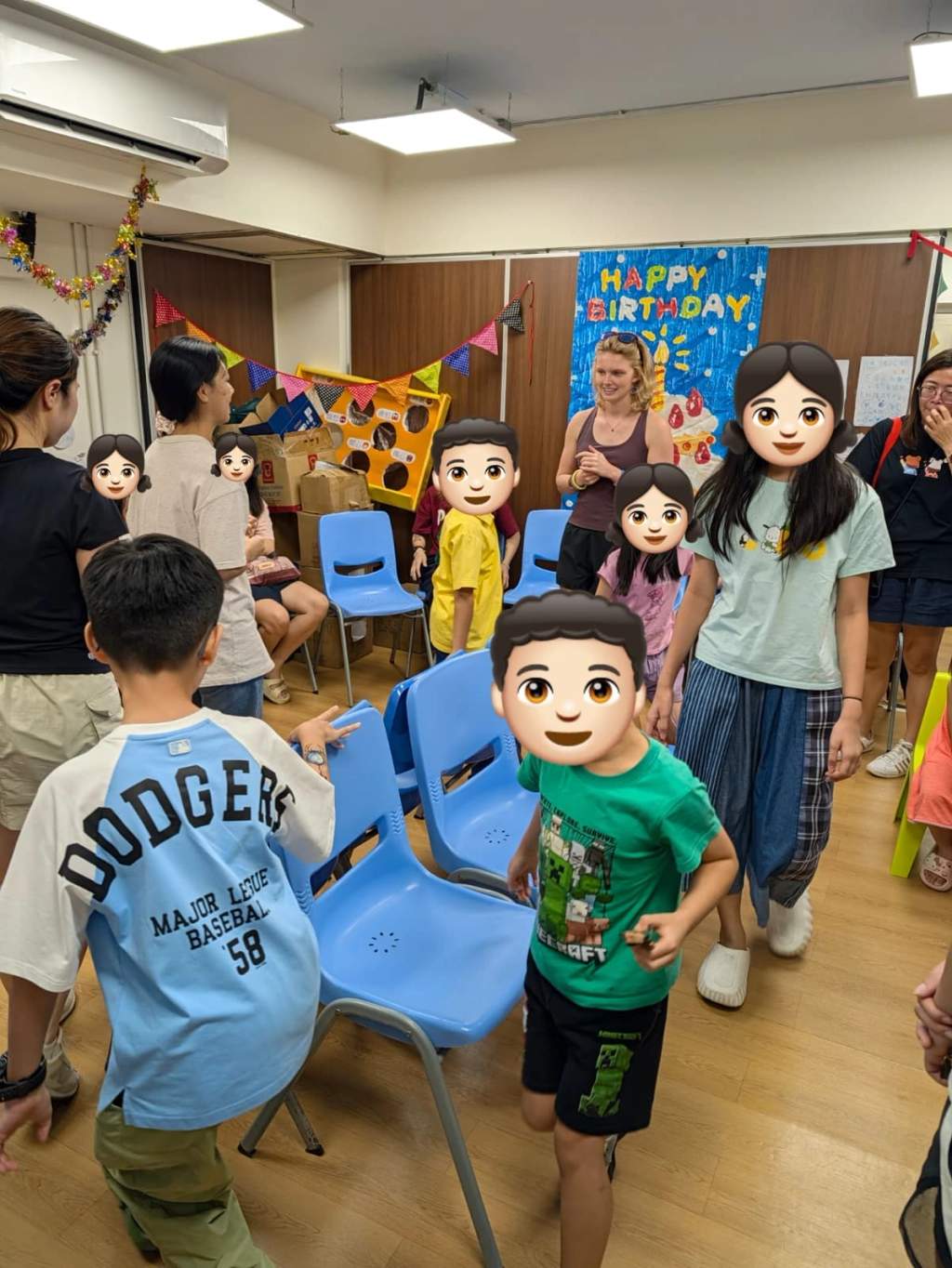Children and volunteers take part in a game among blue chairs.