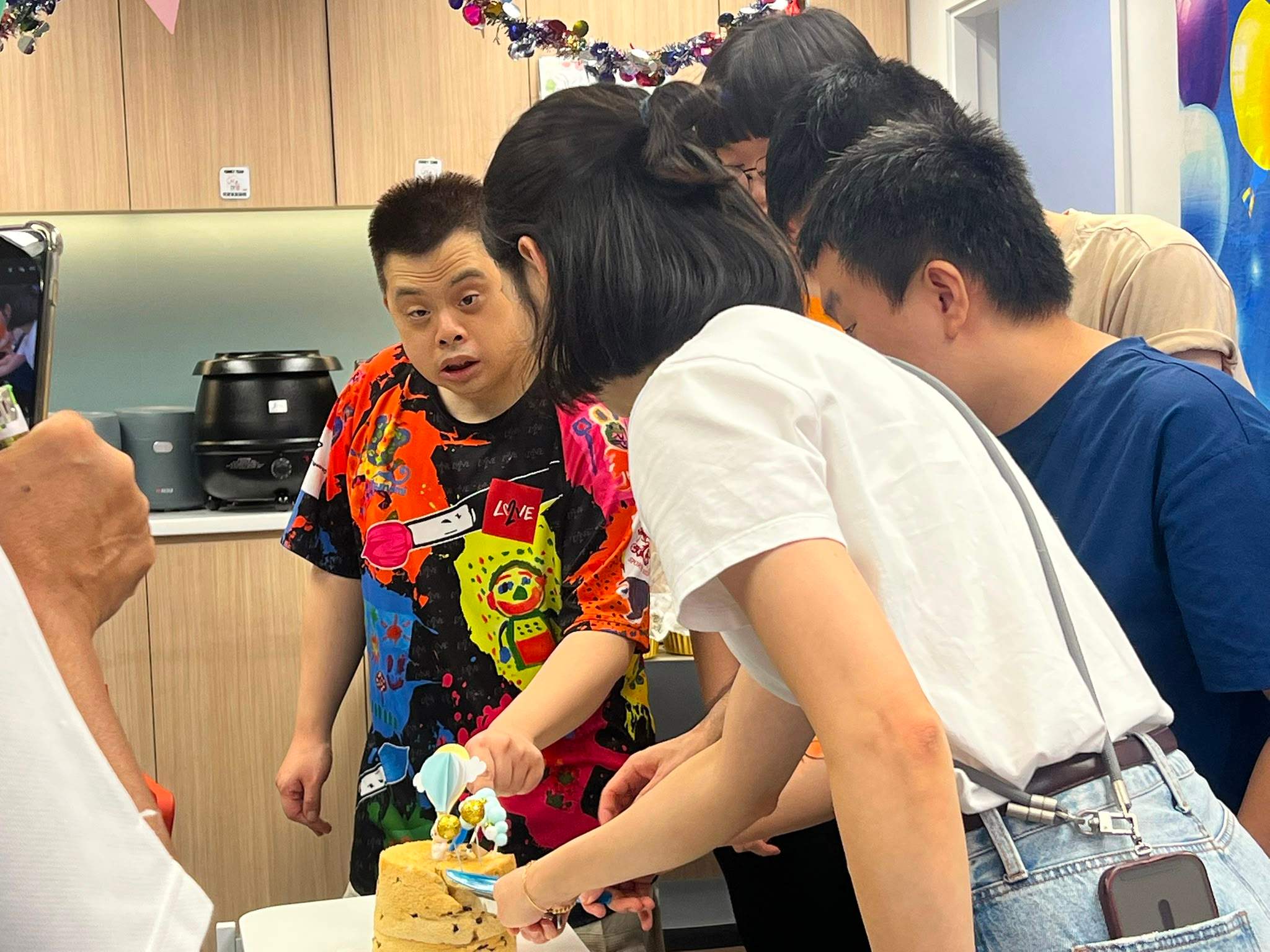 Several people lean over a table to cut the cake.