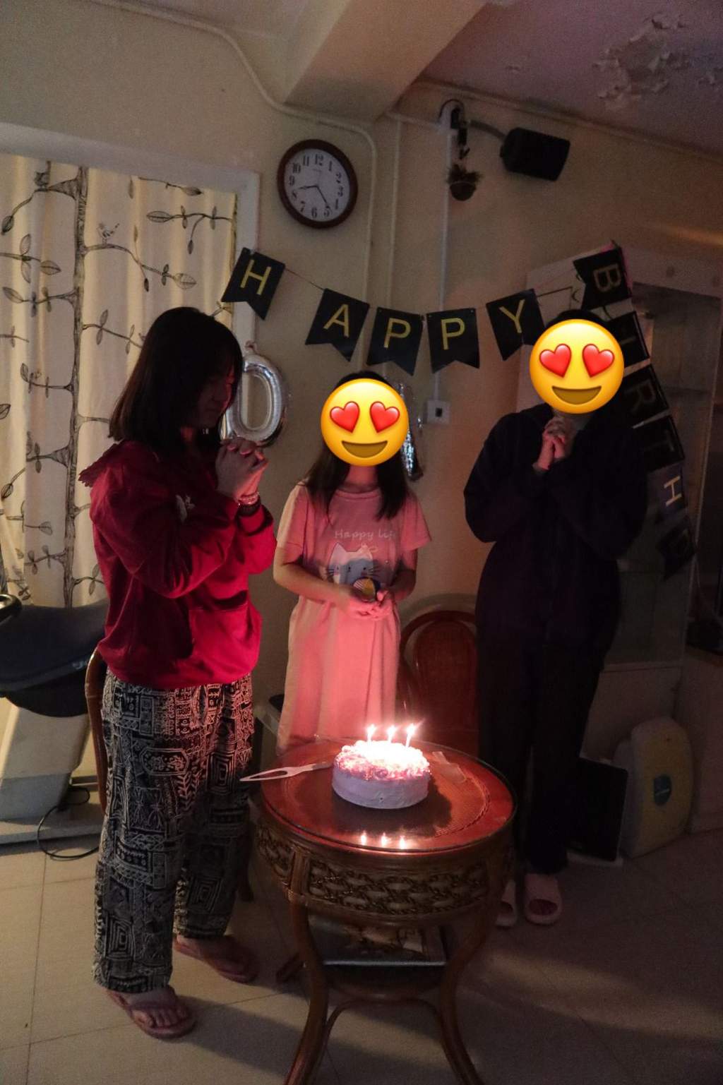 Three people gather around a small cake with glowing candles.