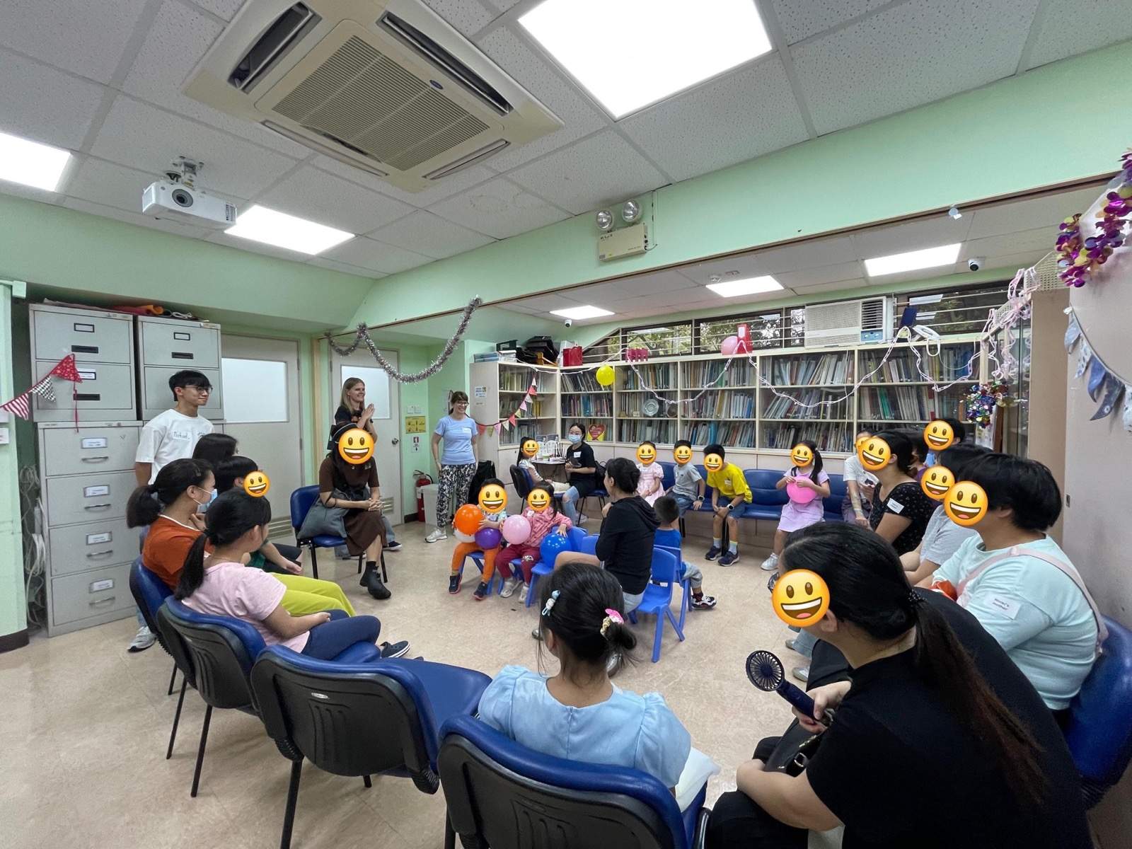 Adults and children sit in a wide circle around the room.