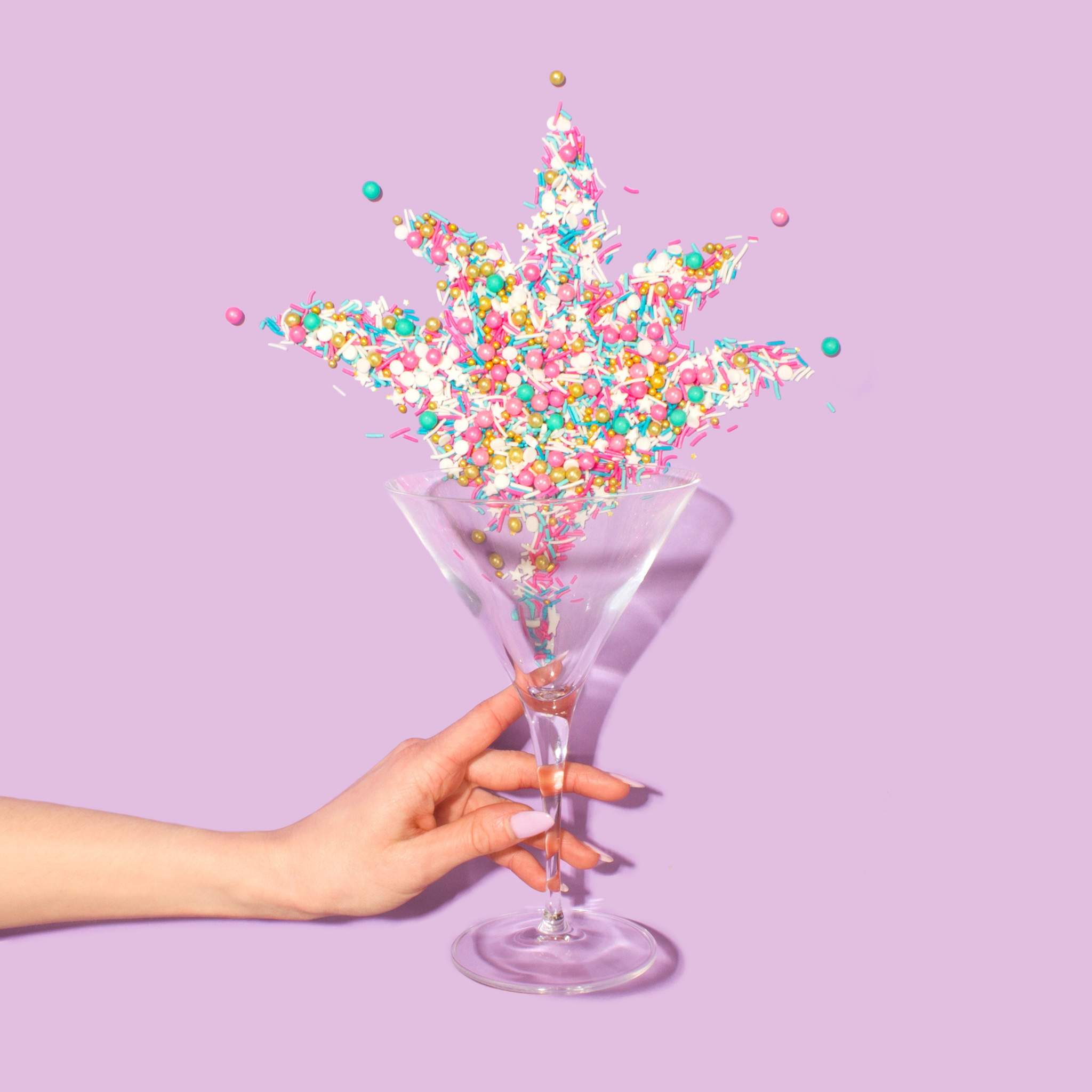 A hand holds a glass filled with colourful star confetti.