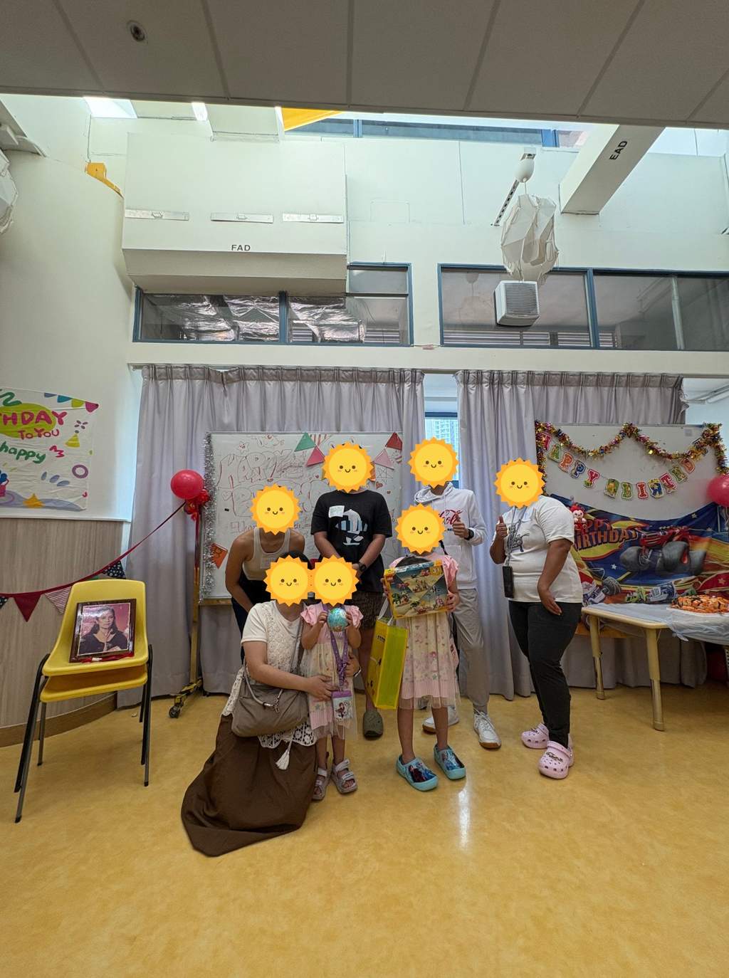 Children and volunteers holding gifts in front of birthday decorations.