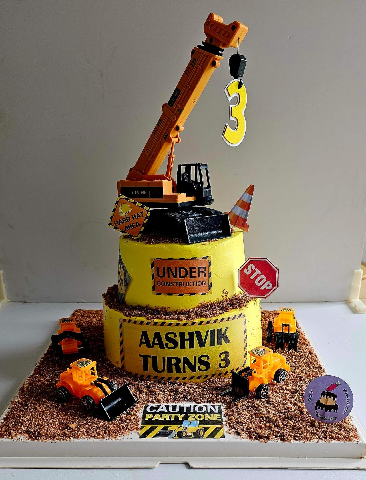 Yellow and black construction-themed cake with a toy crane, construction vehicles and a number three.