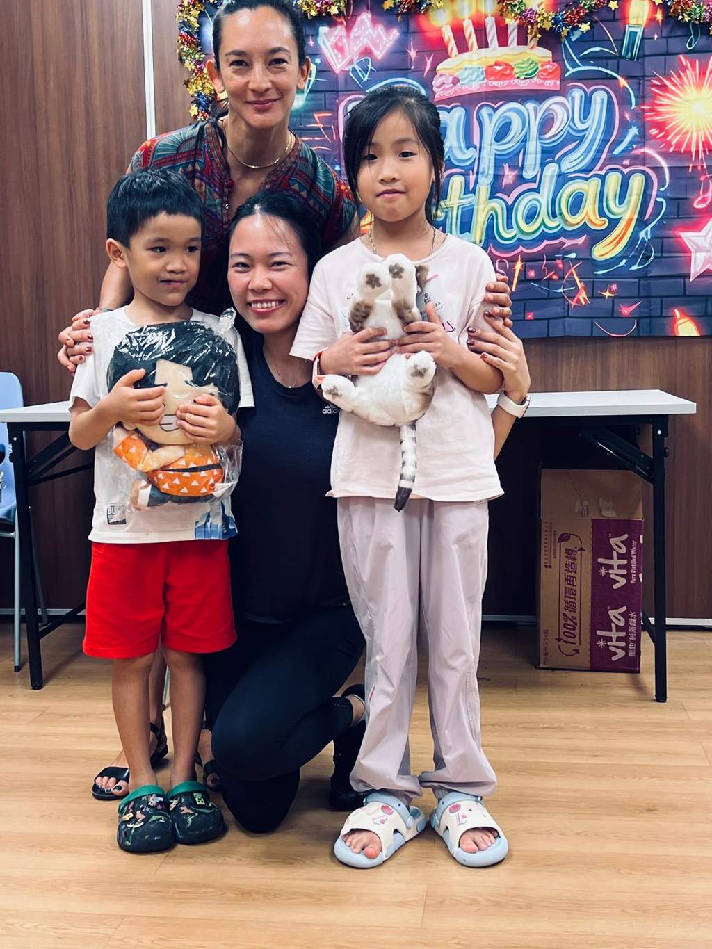 Two children pose between two adults before a birthday backdrop.