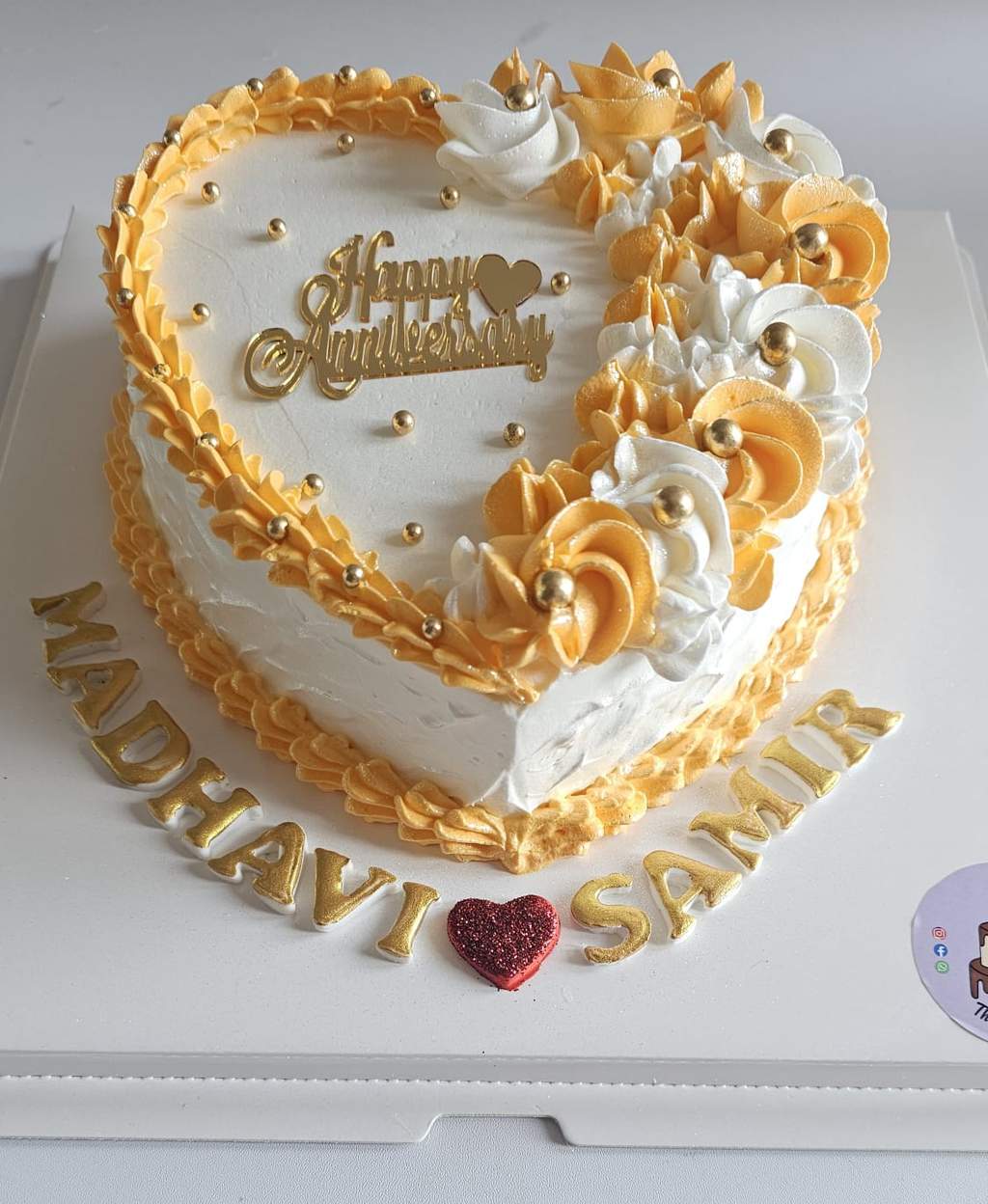 Heart-shaped white and gold anniversary cake decorated with piped rosettes and gold lettering.