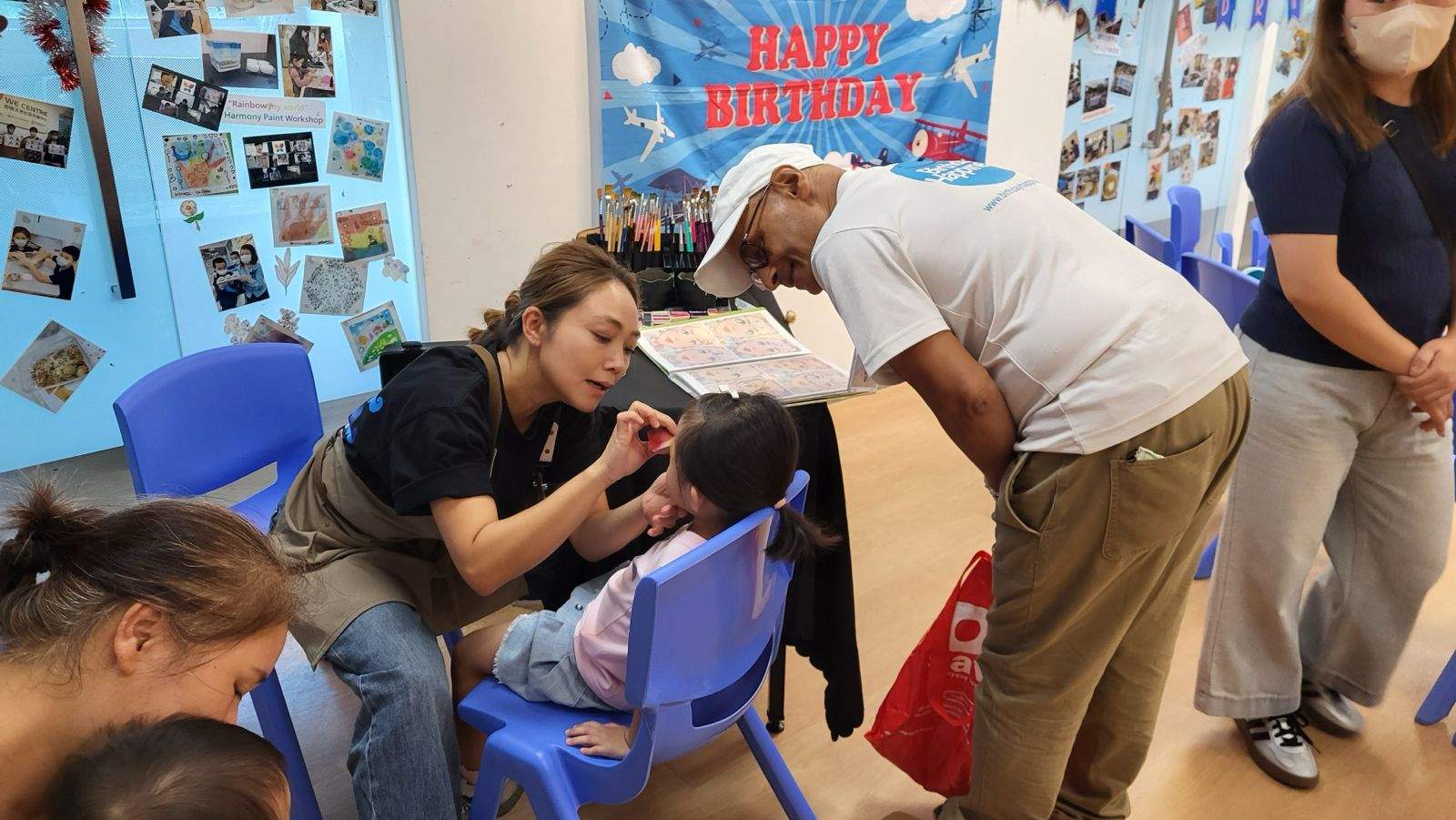 Two adults lean over a seated child during face painting.