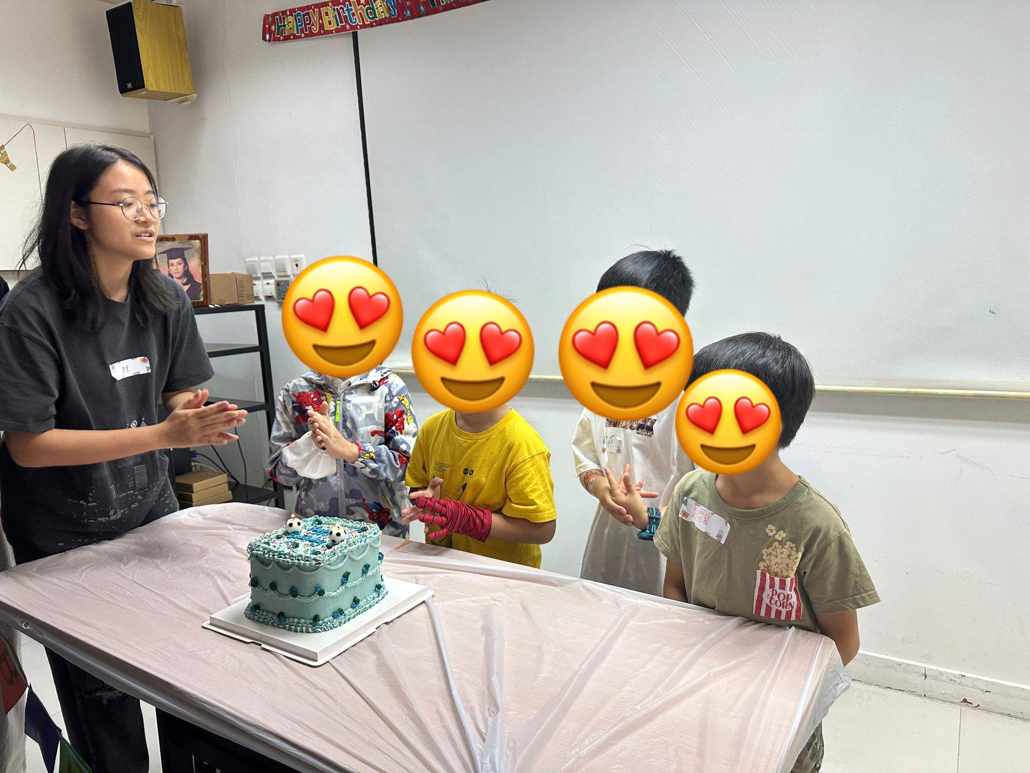 Children gather around a decorated cake on a table.