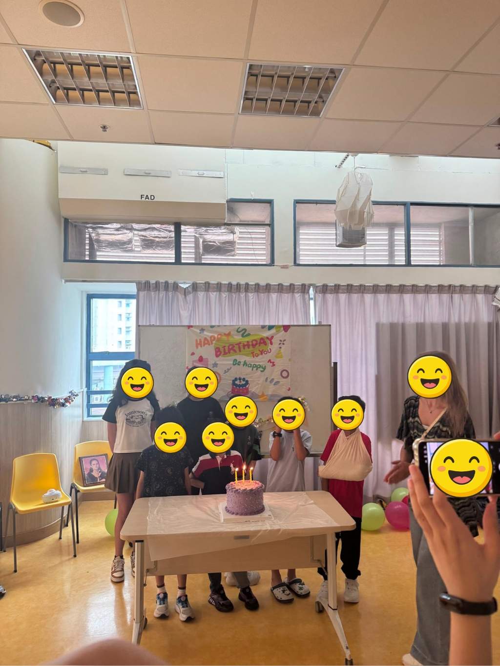 A group gathers behind a candlelit cake and birthday backdrop.