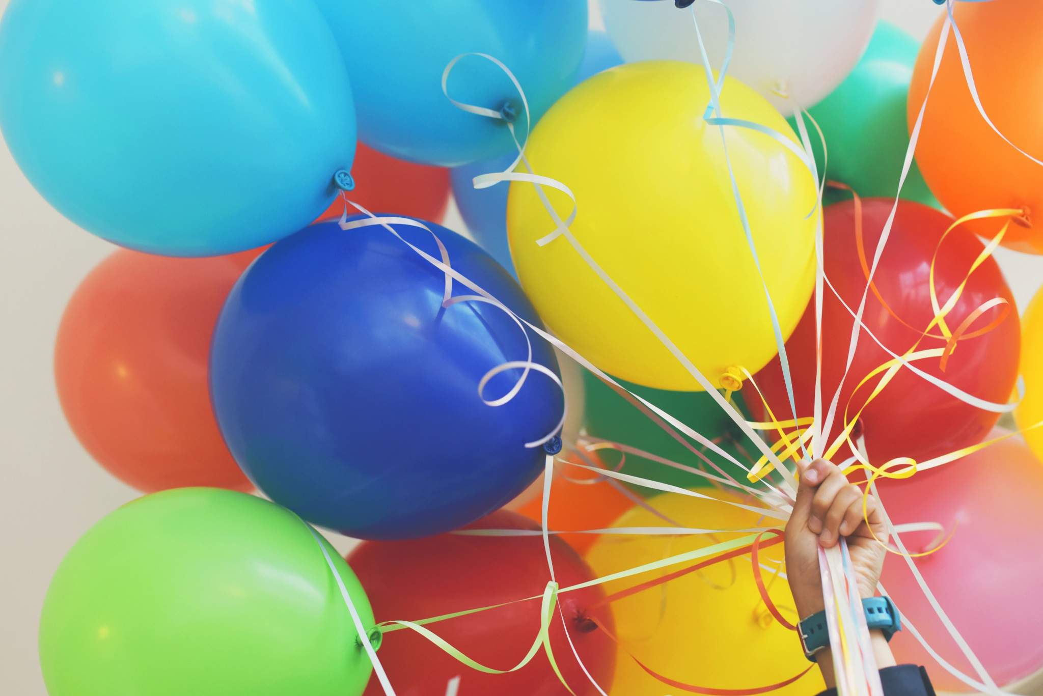 A hand holds a large bunch of colourful balloons.