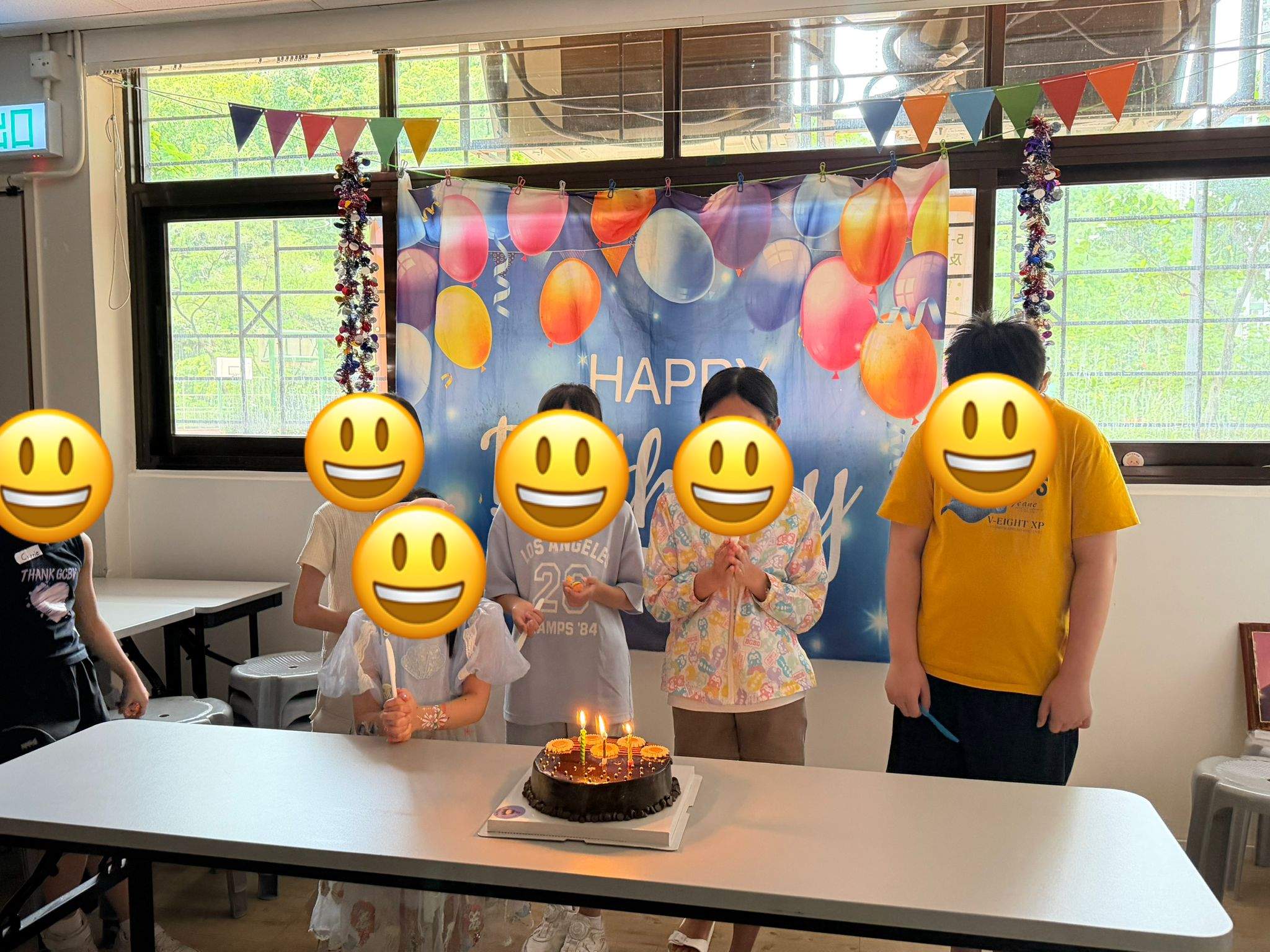 A group gathers behind a candlelit birthday cake and backdrop.