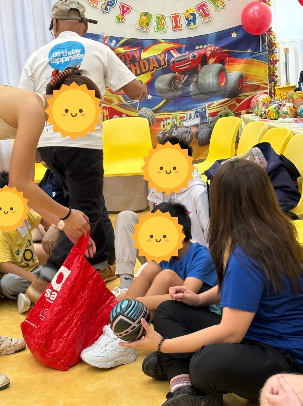 Volunteers handing out gifts to children seated beside yellow chairs.