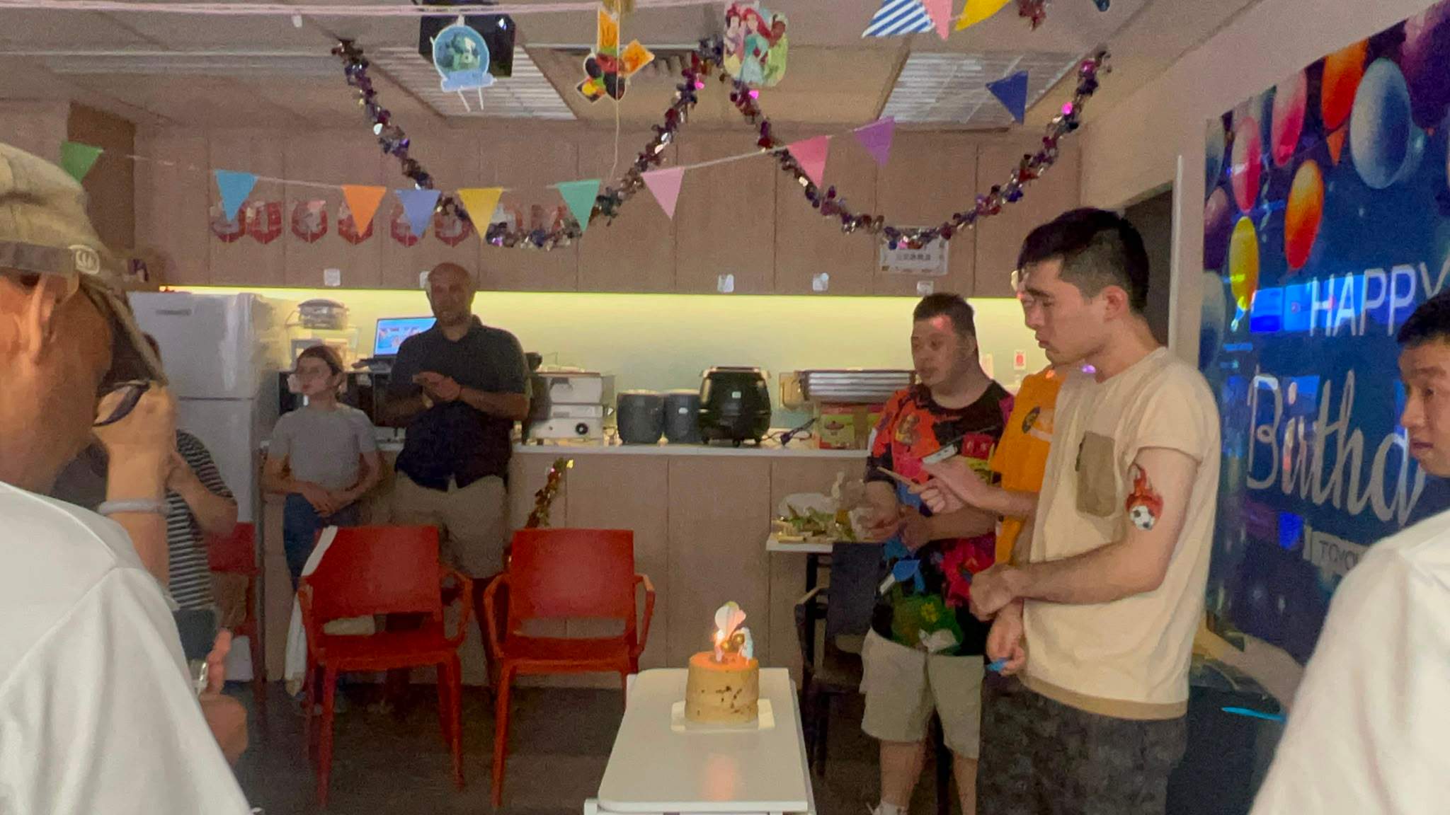 People gather around a small cake in a dimly lit room.