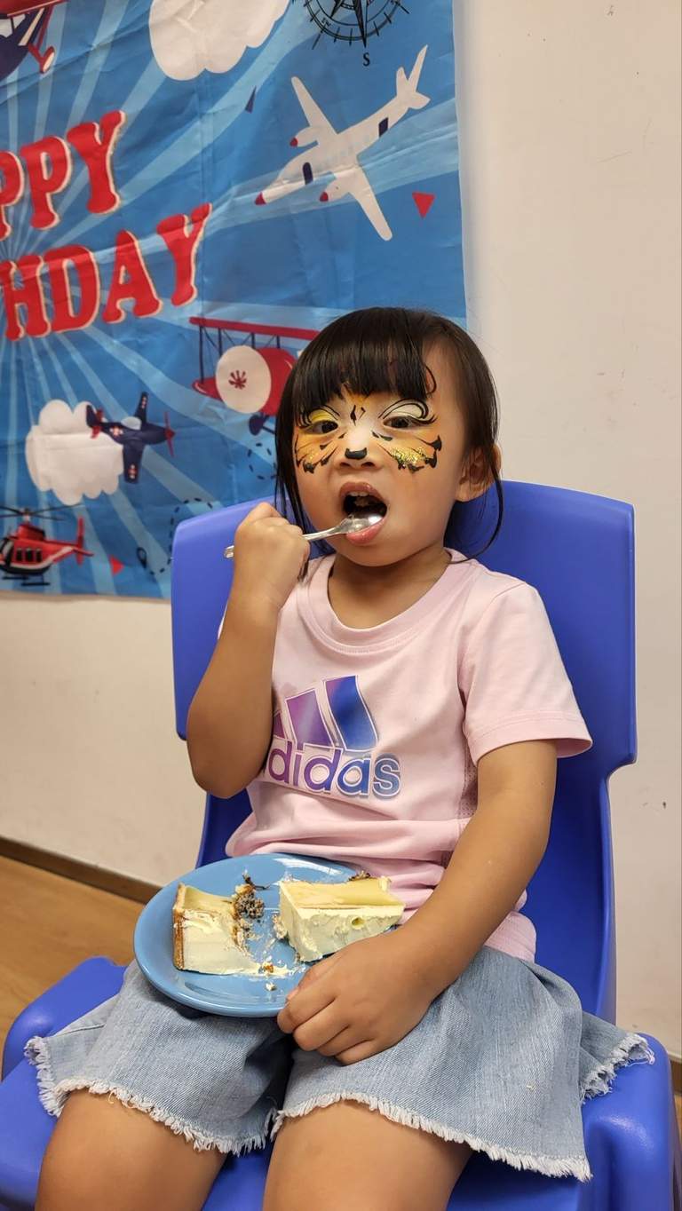 A seated child eats cake from a plate with a spoon.