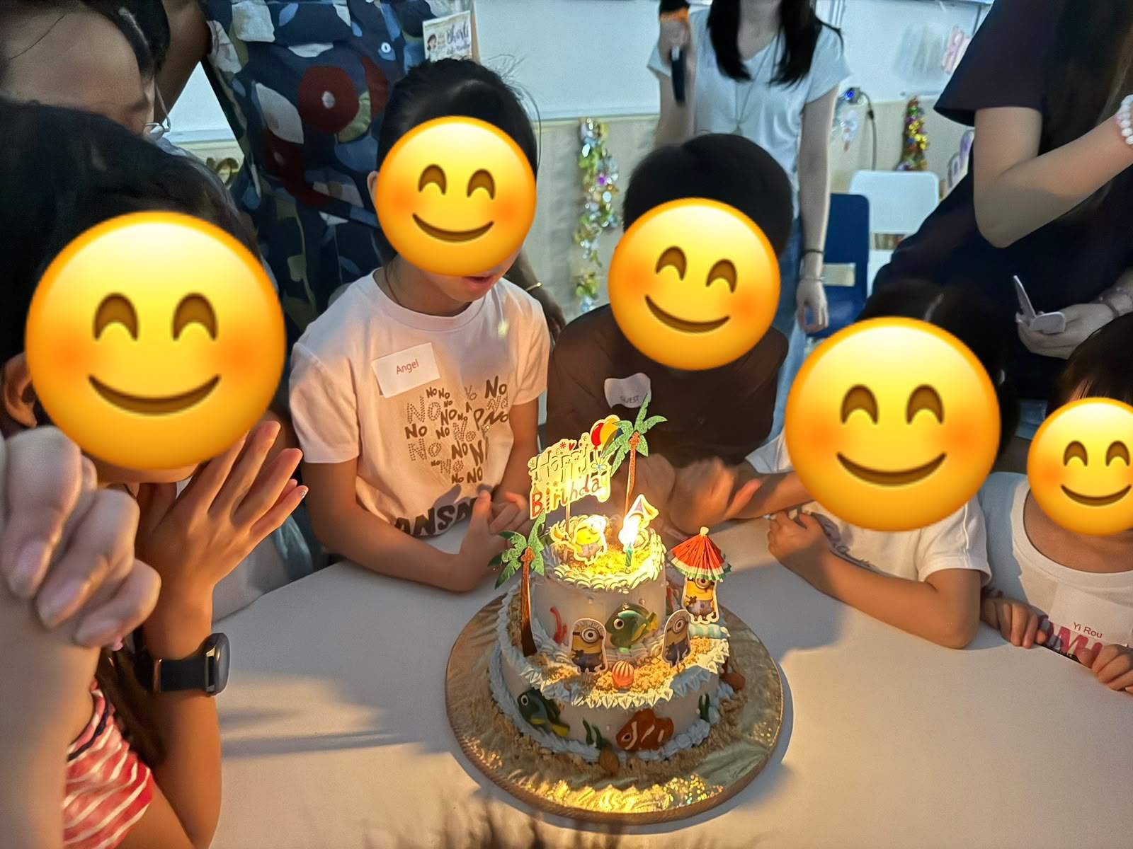 Children gather closely around a decorated cake with candles.