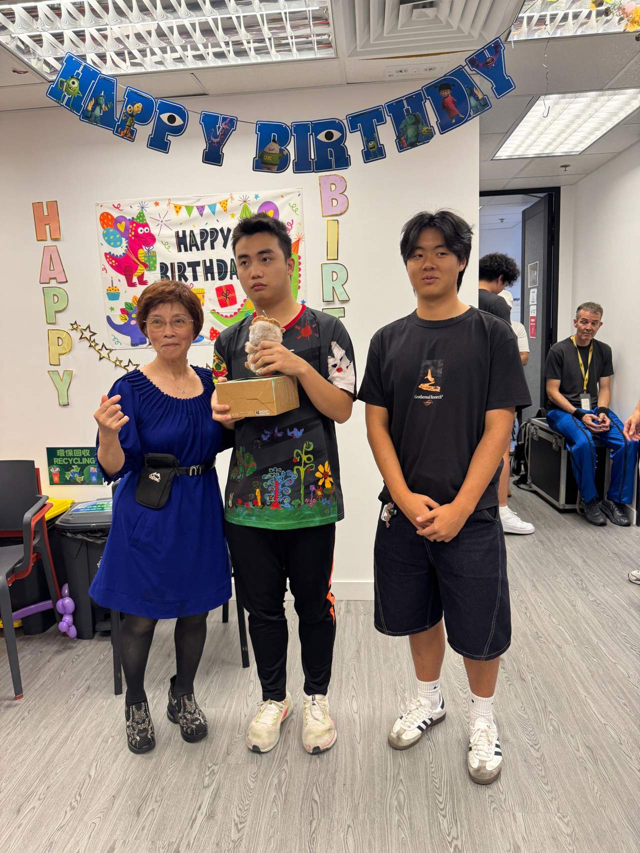 Three people pose together beneath colourful birthday decorations.