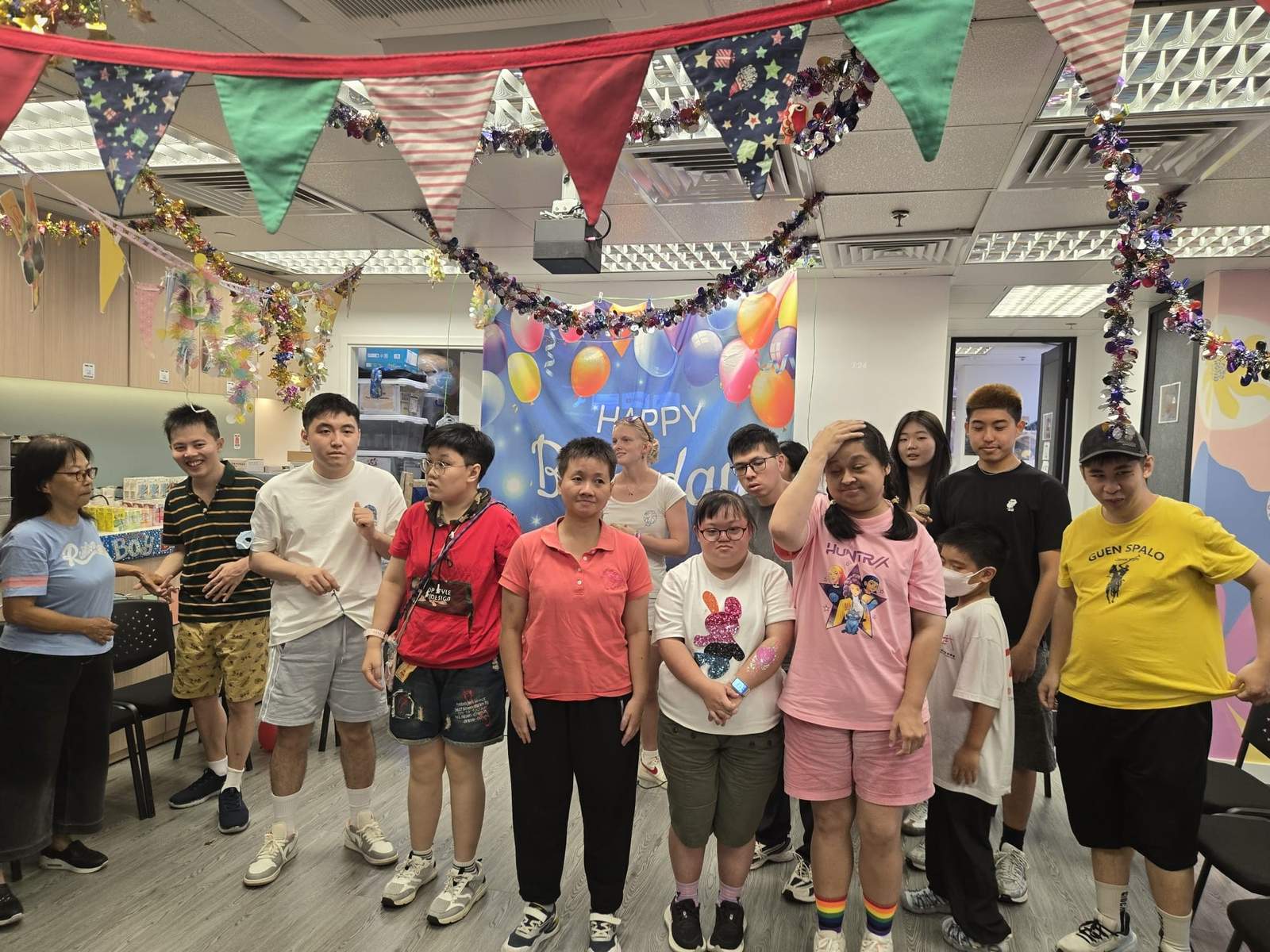 A large group stands together beneath colourful party decorations.