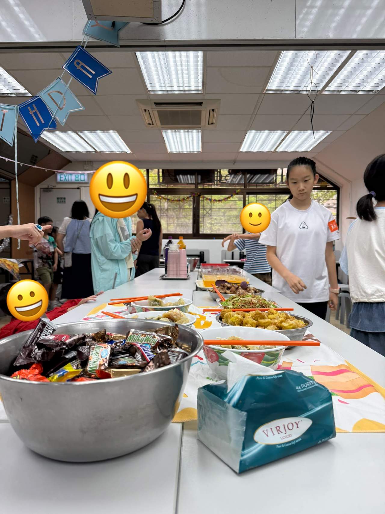 Children stand beside a table covered with snacks and drinks.