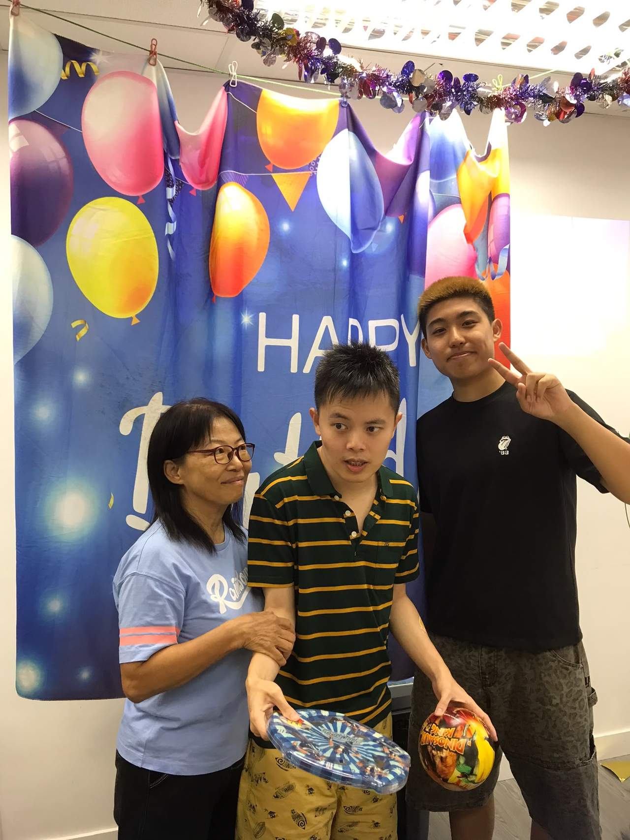 Three attendees display gifts beside a birthday backdrop.