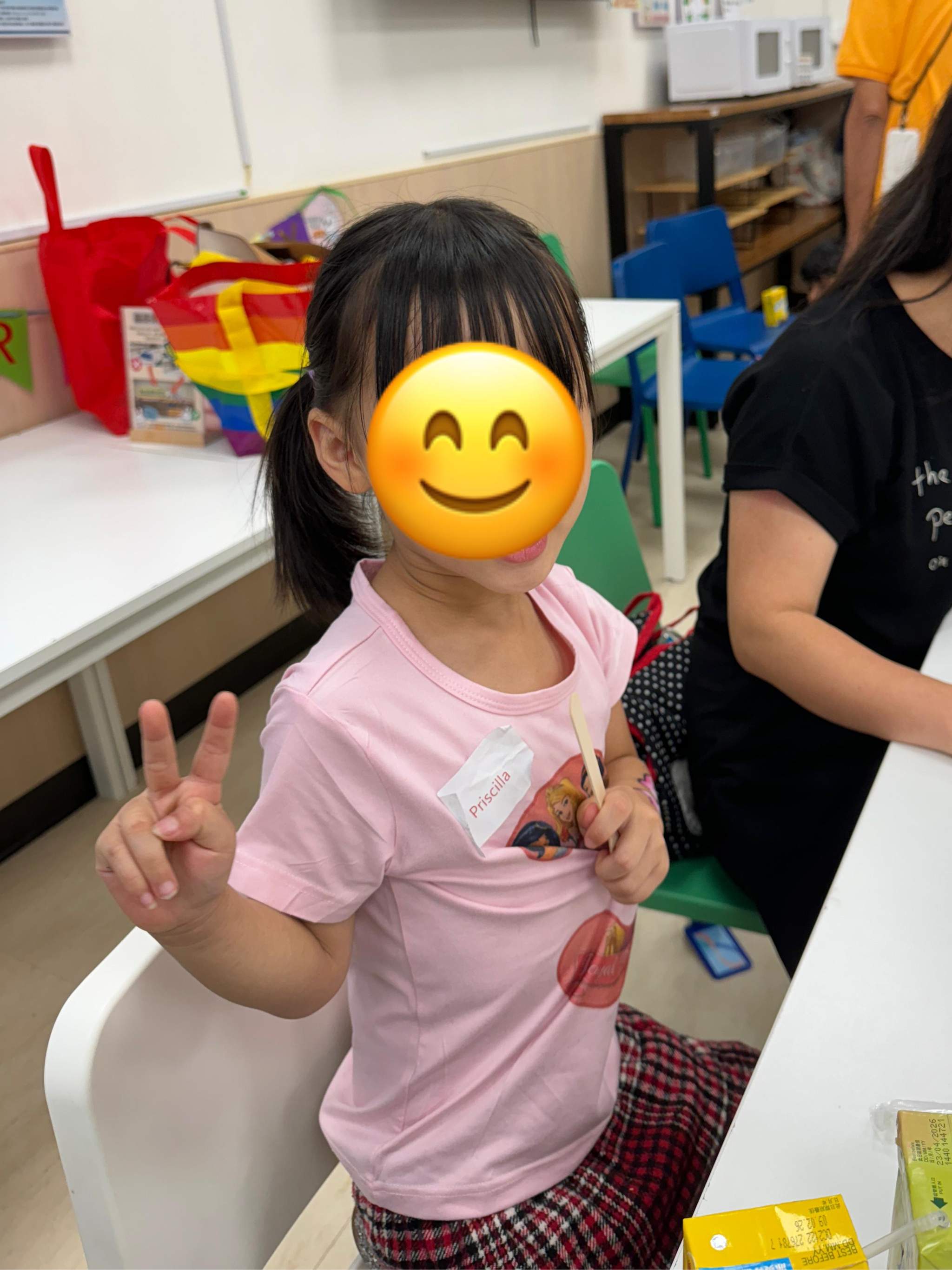 A child stands beside a table and gestures towards the camera.
