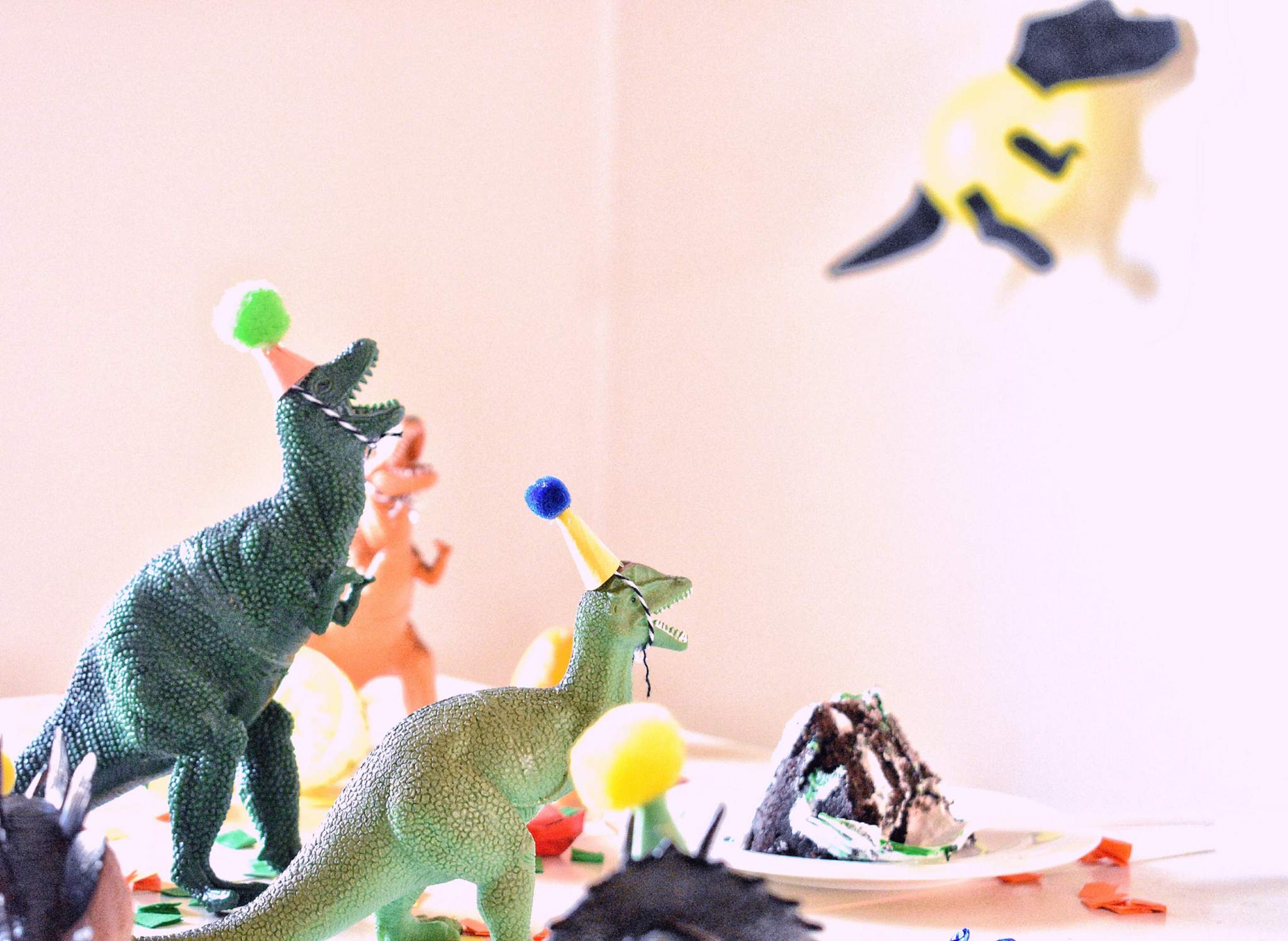 Toy dinosaurs and colourful party picks stand against a pale background.