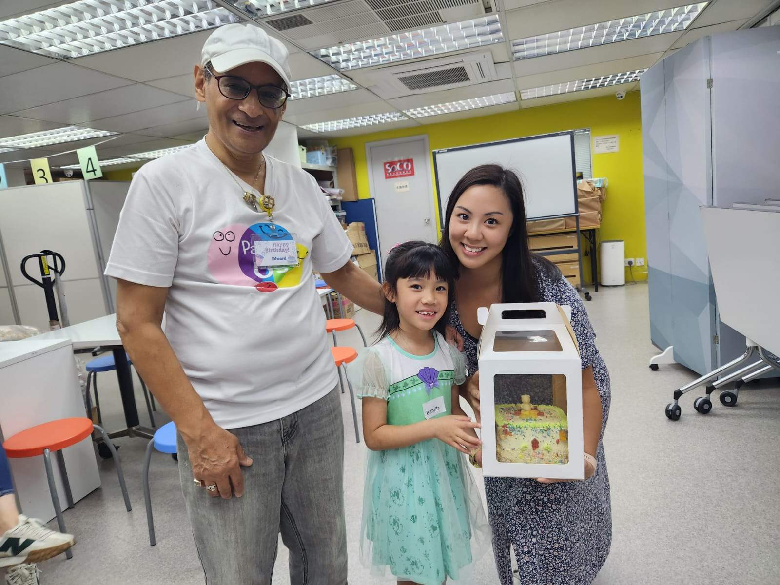 Two adults pose with a child holding a boxed cake.