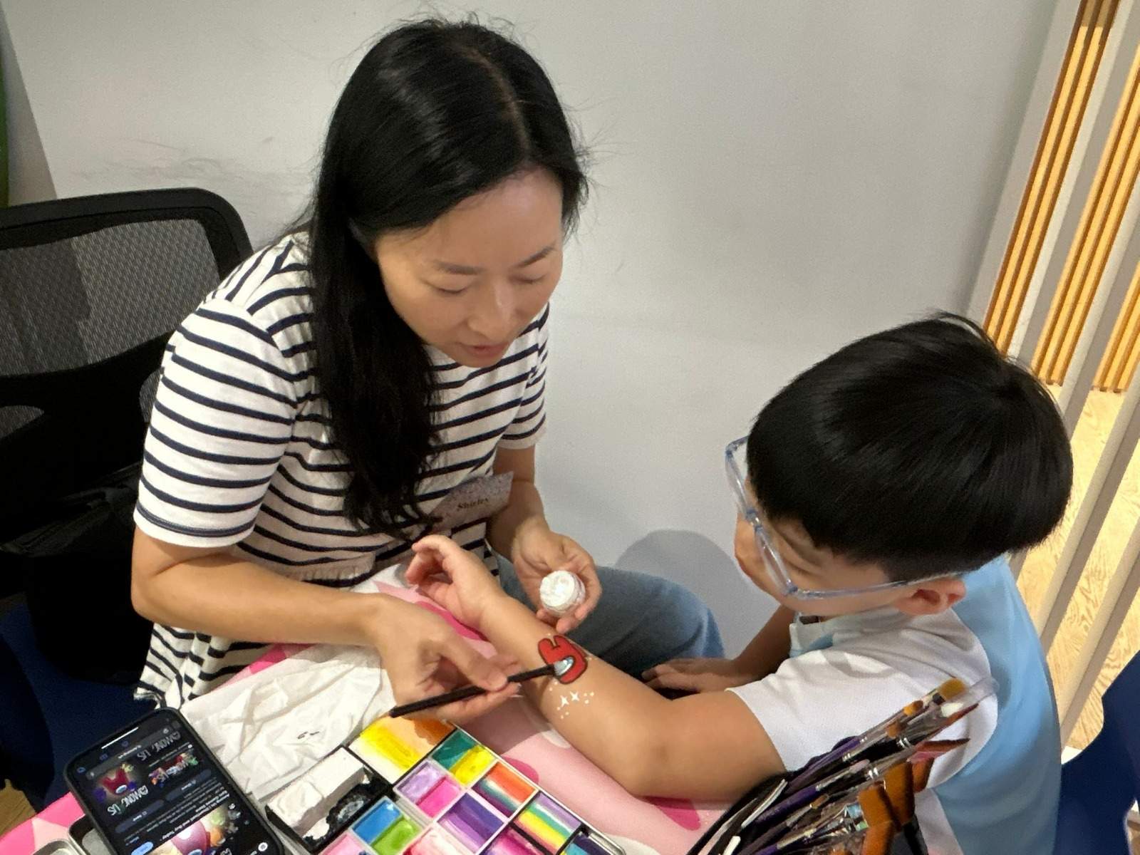 An adult paints a seated child's forearm at a table.