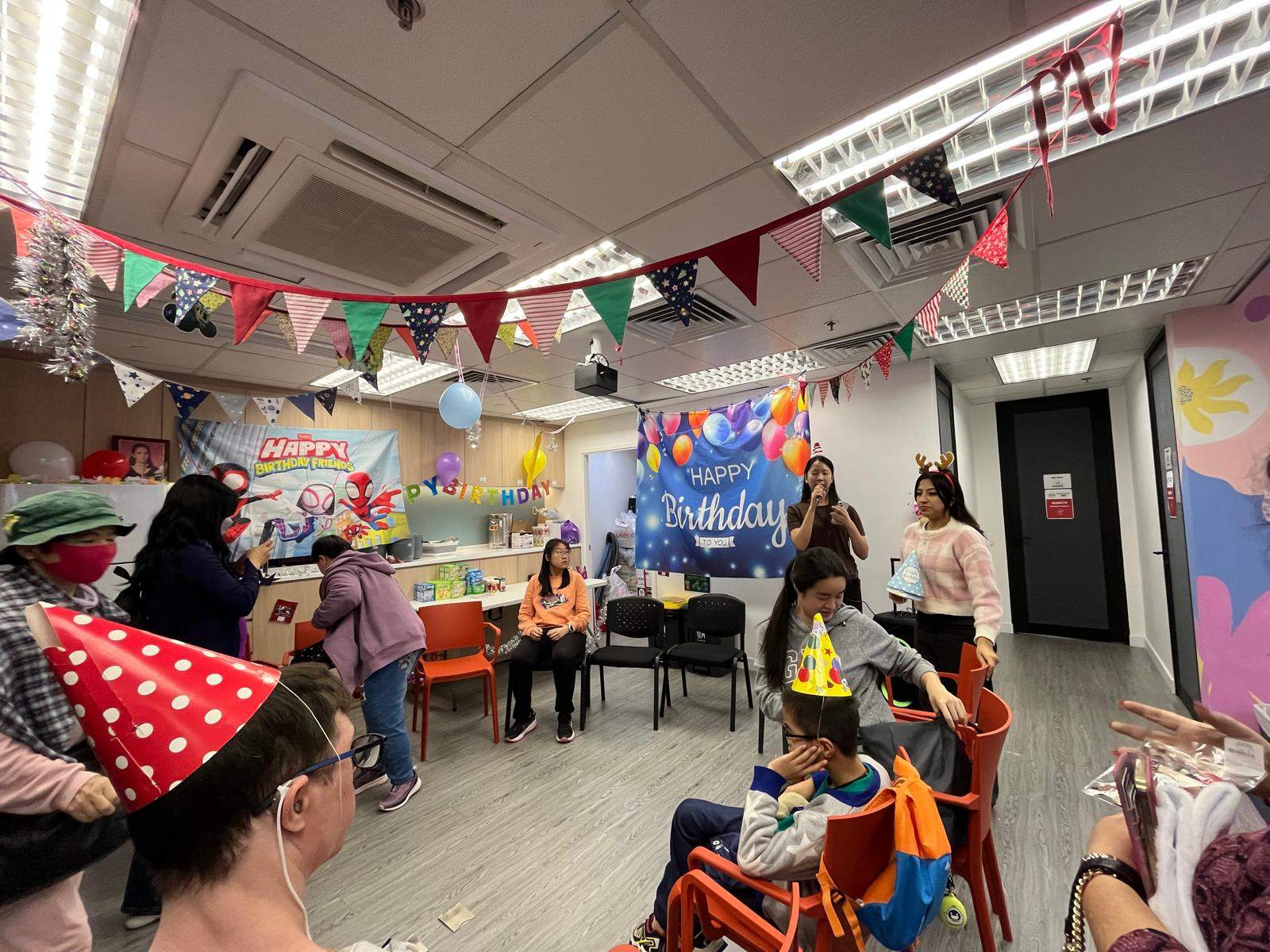 A costumed adult addresses people seated around the room.