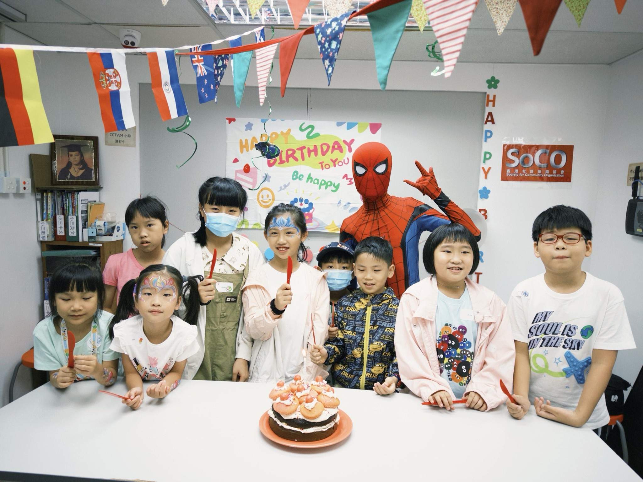 Children gather behind a cake beside a costumed performer.