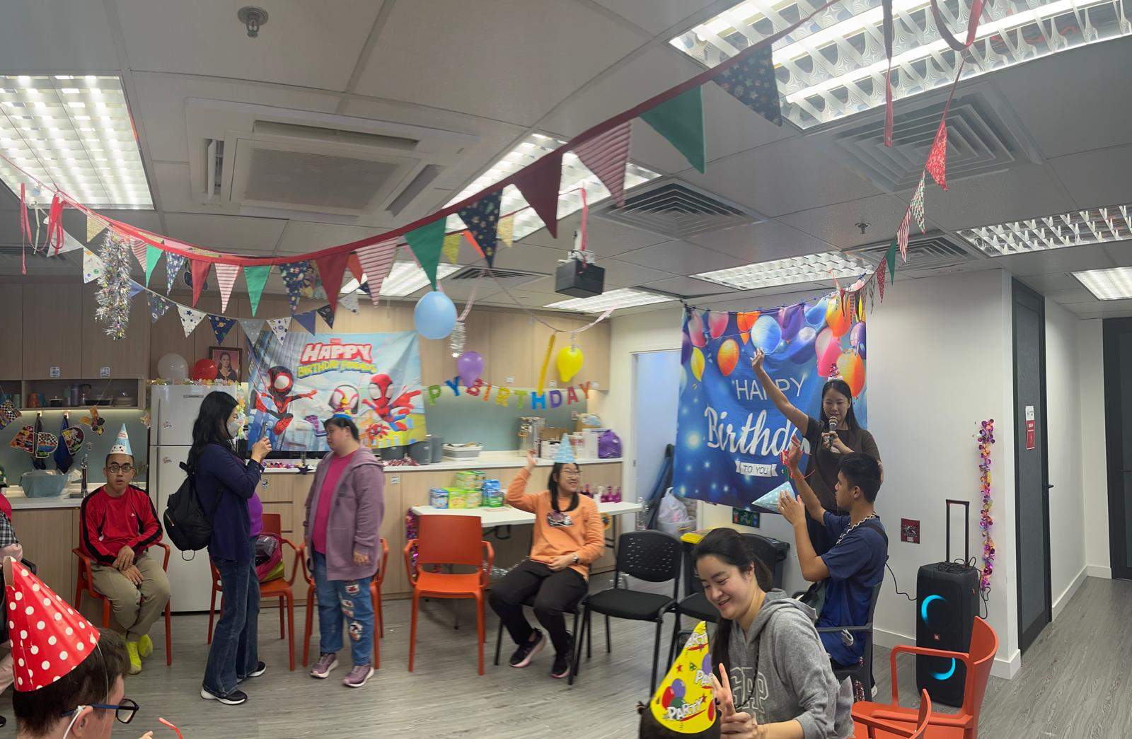 People stand and sit beneath bunting and balloon decorations.