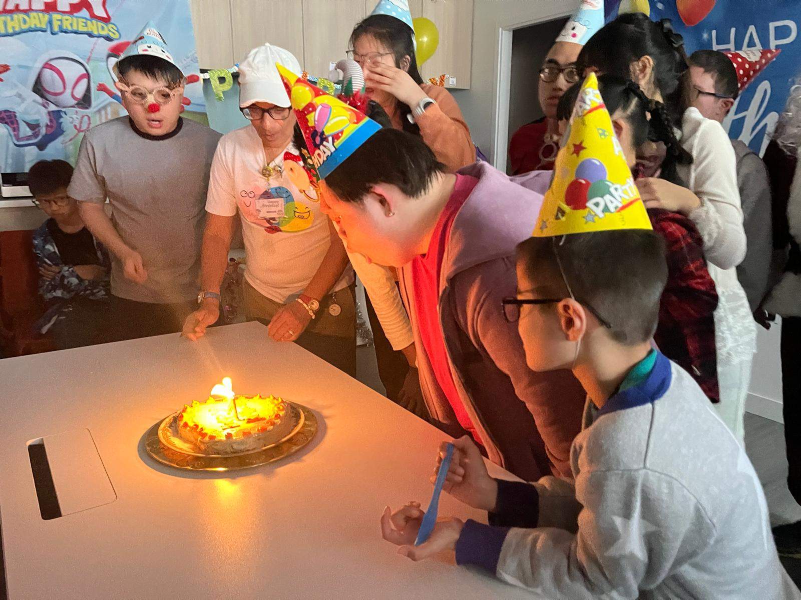 People gather around a candlelit cake while wearing party hats.